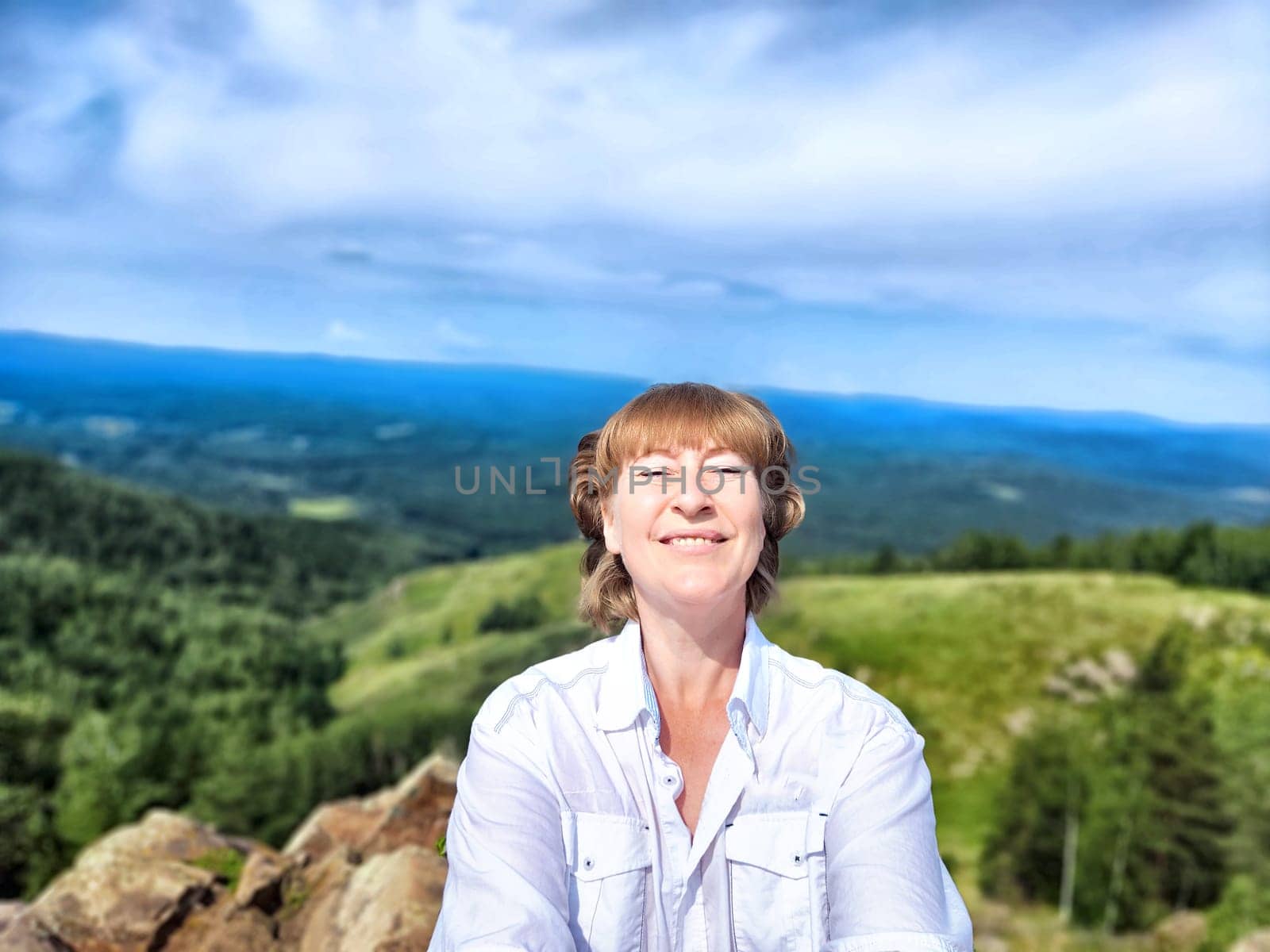 A blogger happily takes a selfie with breathtaking mountain views in the background while enjoying her adventure in nature