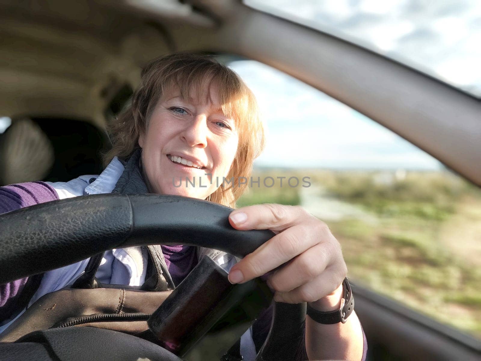 Middle aged woman in a car taking a selfie while enjoying a drive. Female mature driver posing inside car. Funny happy tourist girl in alone travel