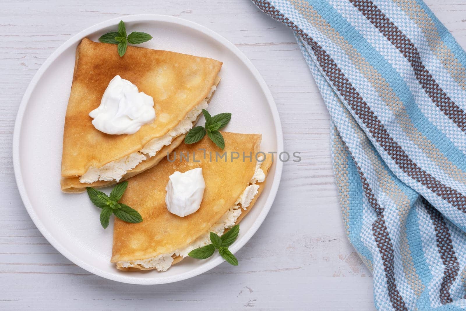 Thin pancakes, russian blini or french crepes with cottage cheese. Tasty homemade breakfast. Top view, copy space.