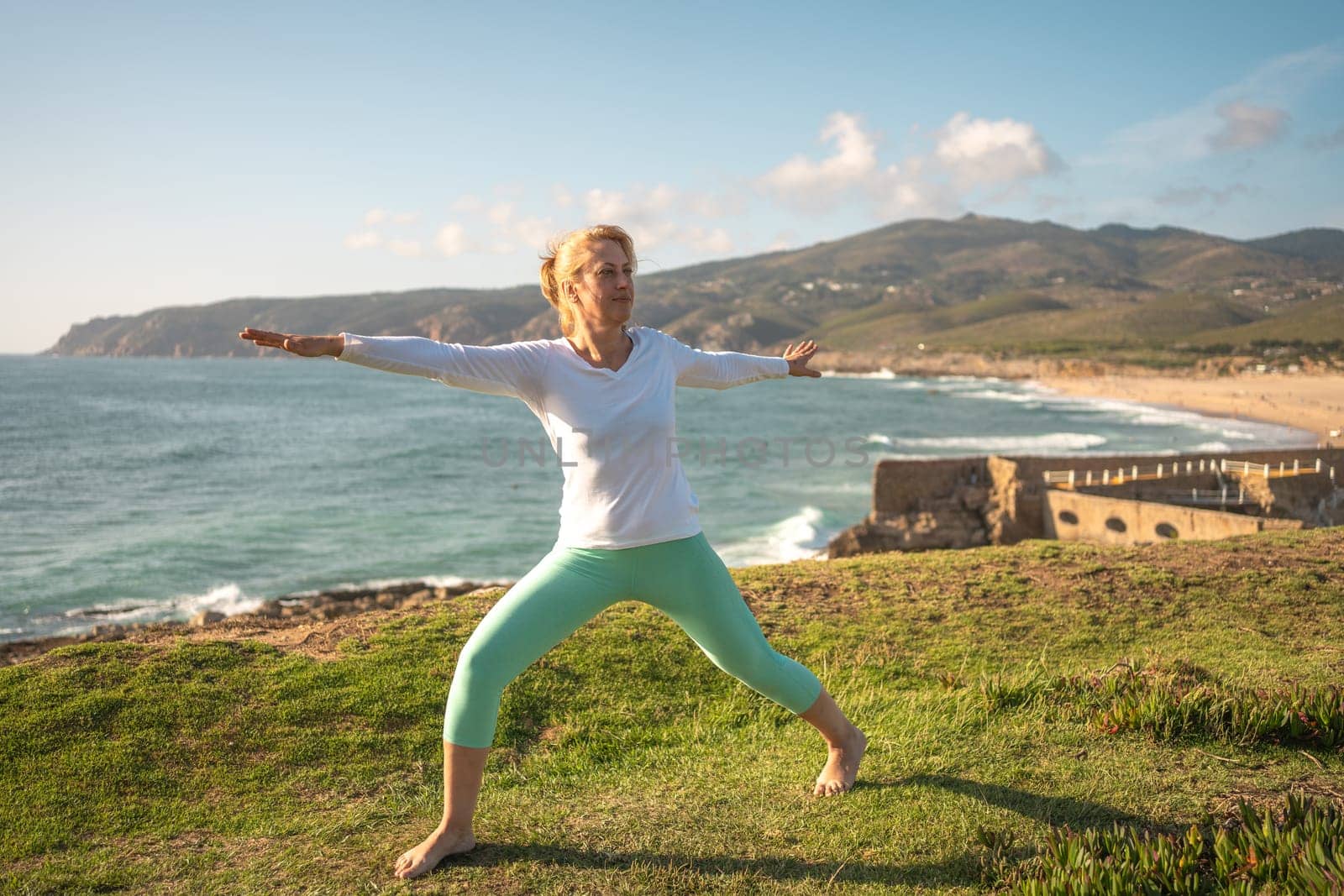 Senior woman doing yoga performing asanas on ocean shore. Active retired female taking care her body and enjoying life in sunny morning. Retirement, relaxation, vacation, healthy senior lifestyle