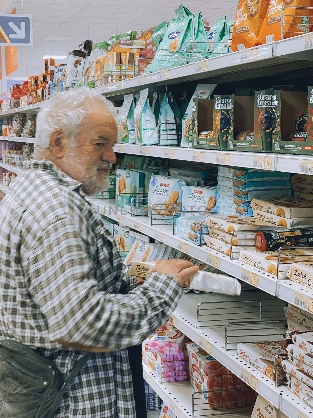 Cremona, Lombardy, Italy October 15th 2024 Elderly man shopping for cookies in a supermarket, carefully checking the packaging information before making a purchase