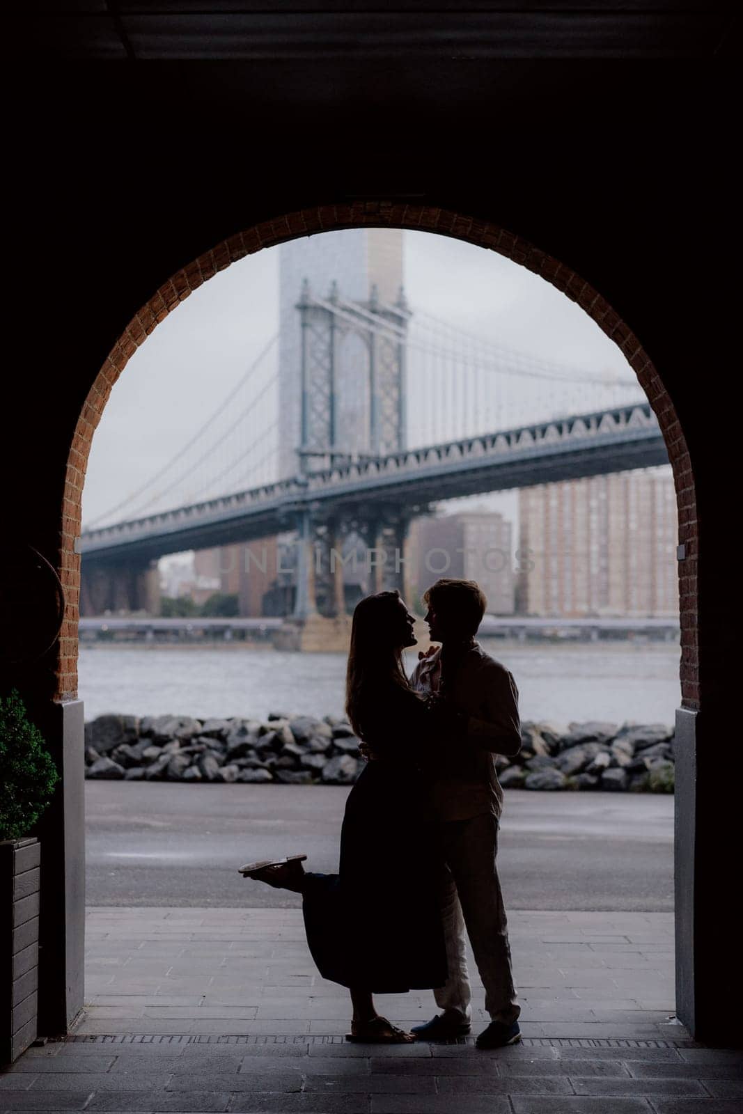 A loving couple is sharing a beautiful tender moment, beautifully silhouetted against a lovely Manhattan bridge backdrop in New York.