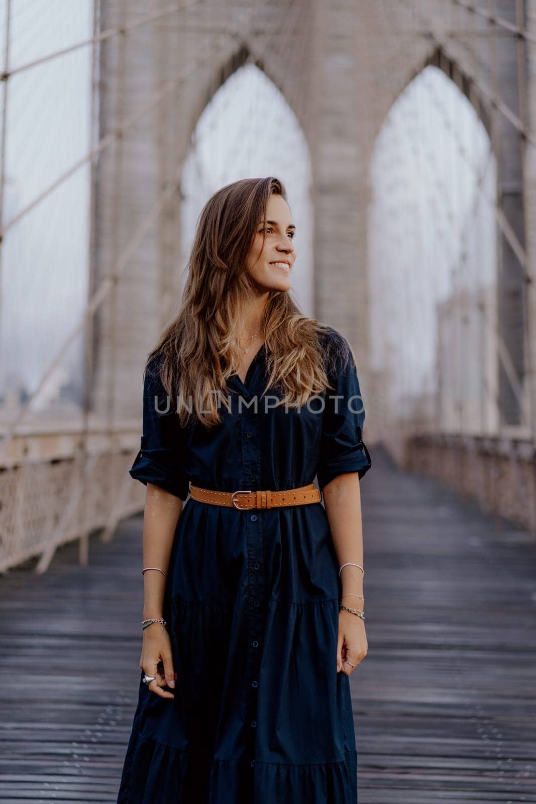 A young woman poses in a stylish dress on Brooklyn Bridge, showcasing a blend of elegance and urban charm.