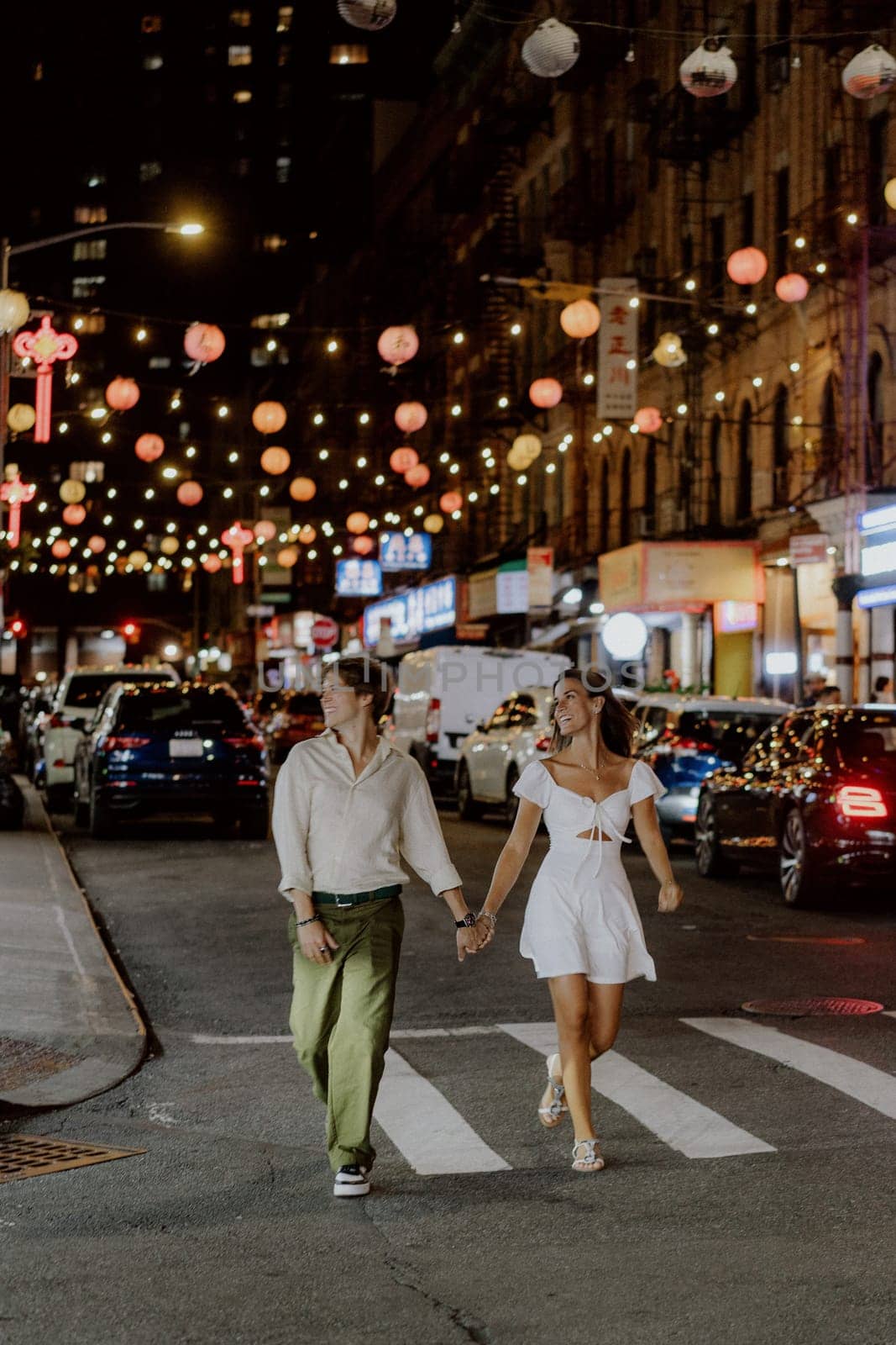 A charming couple leisurely strolls through a bustling city street, which is beautifully adorned with vibrant lanterns