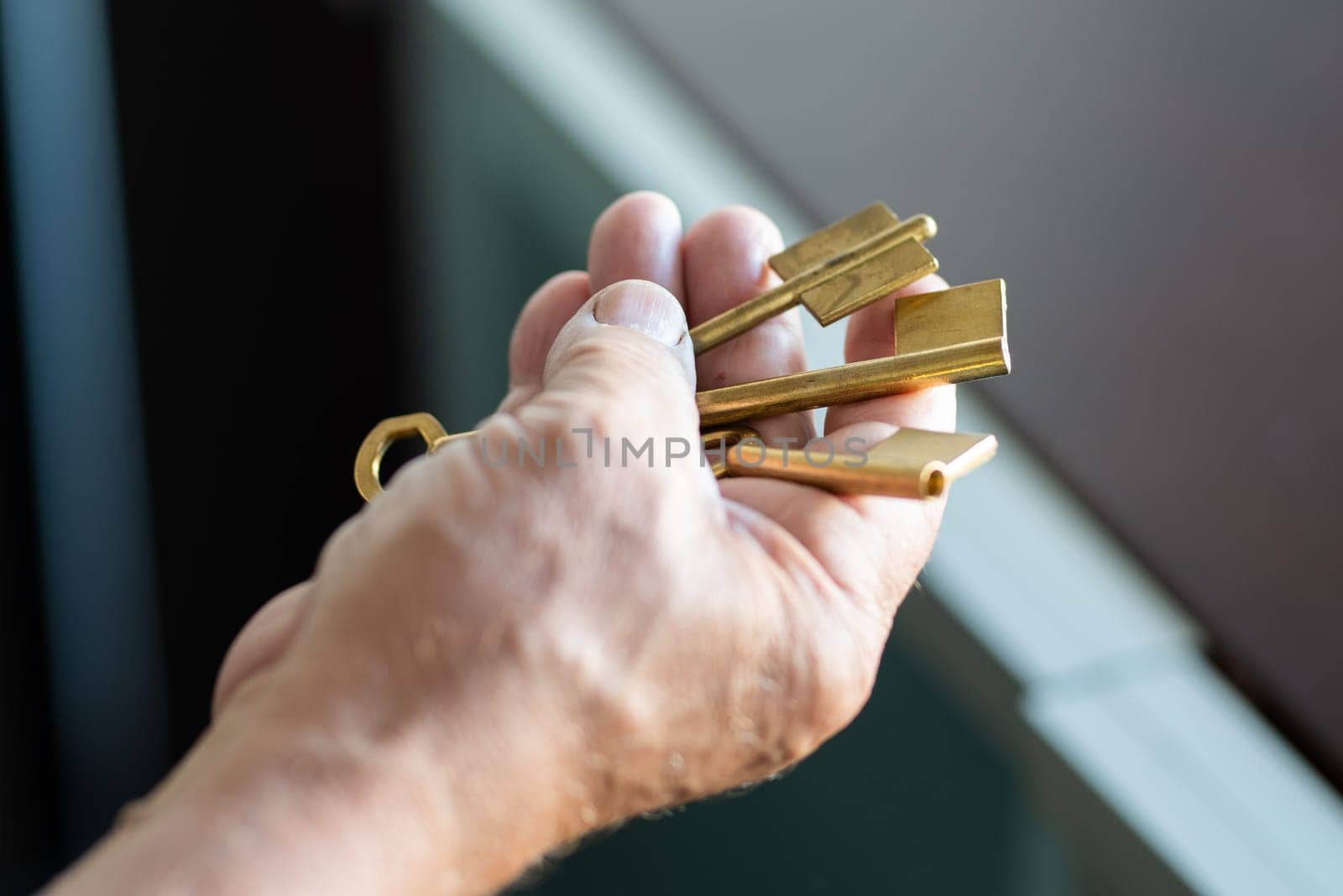 Man holding key with metallic keychain on house background, closeup. High quality photo
