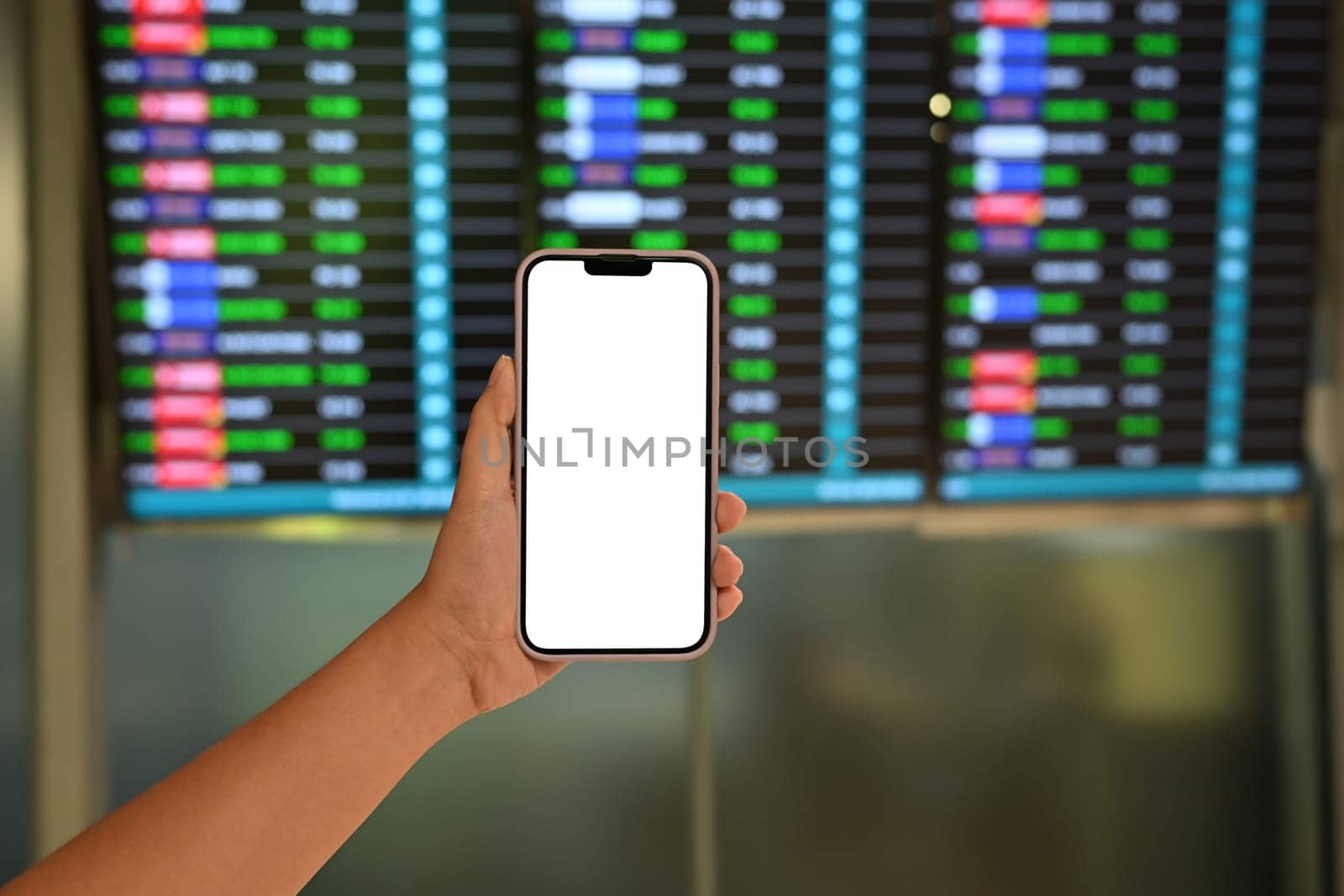 Traveler holding a smartphone with blank screen against airport flight board.