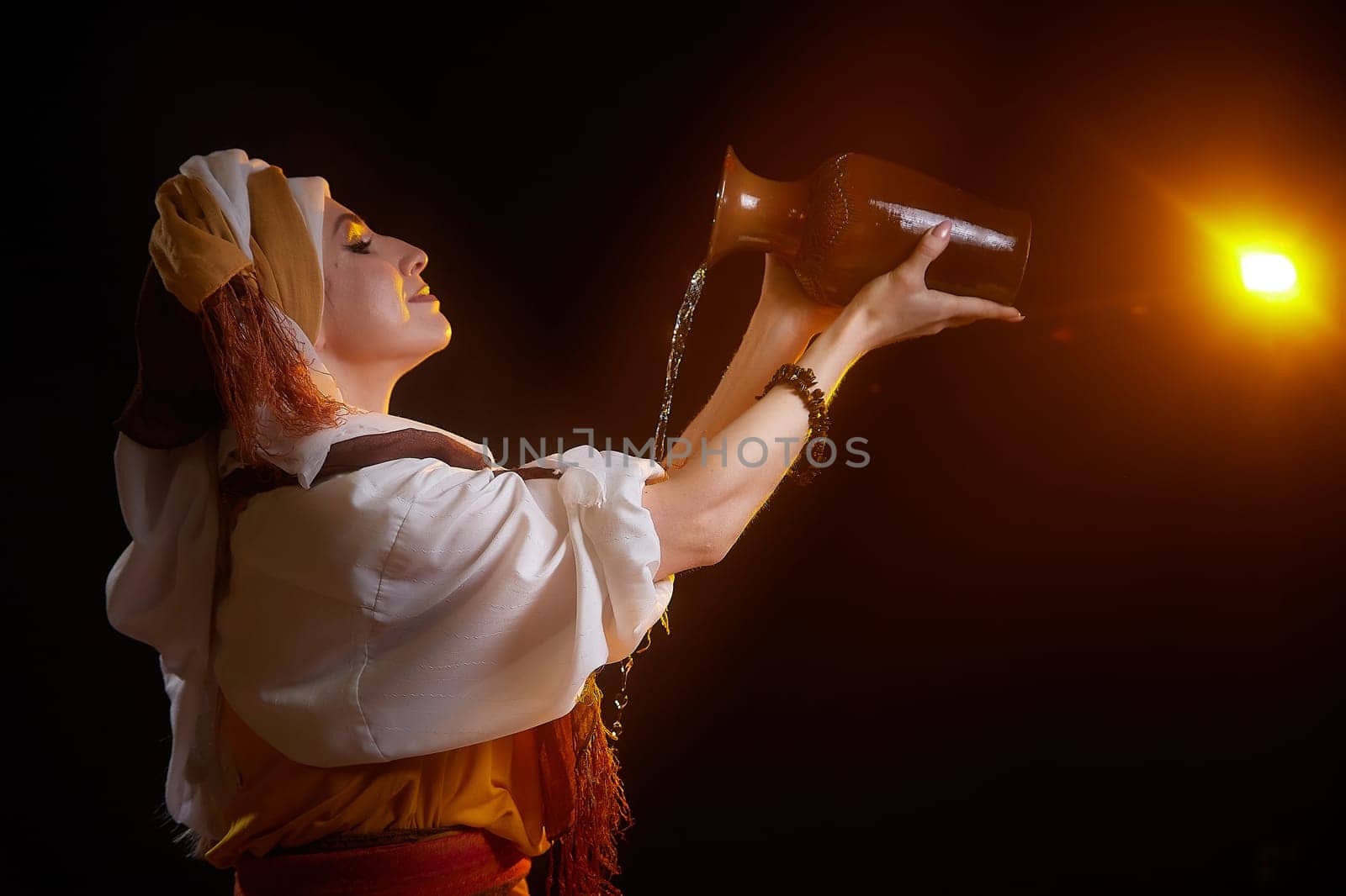 A girl dressed in ornate national clothing showcases a water drawing ritual, embodying the character of Rebekah at twilight.