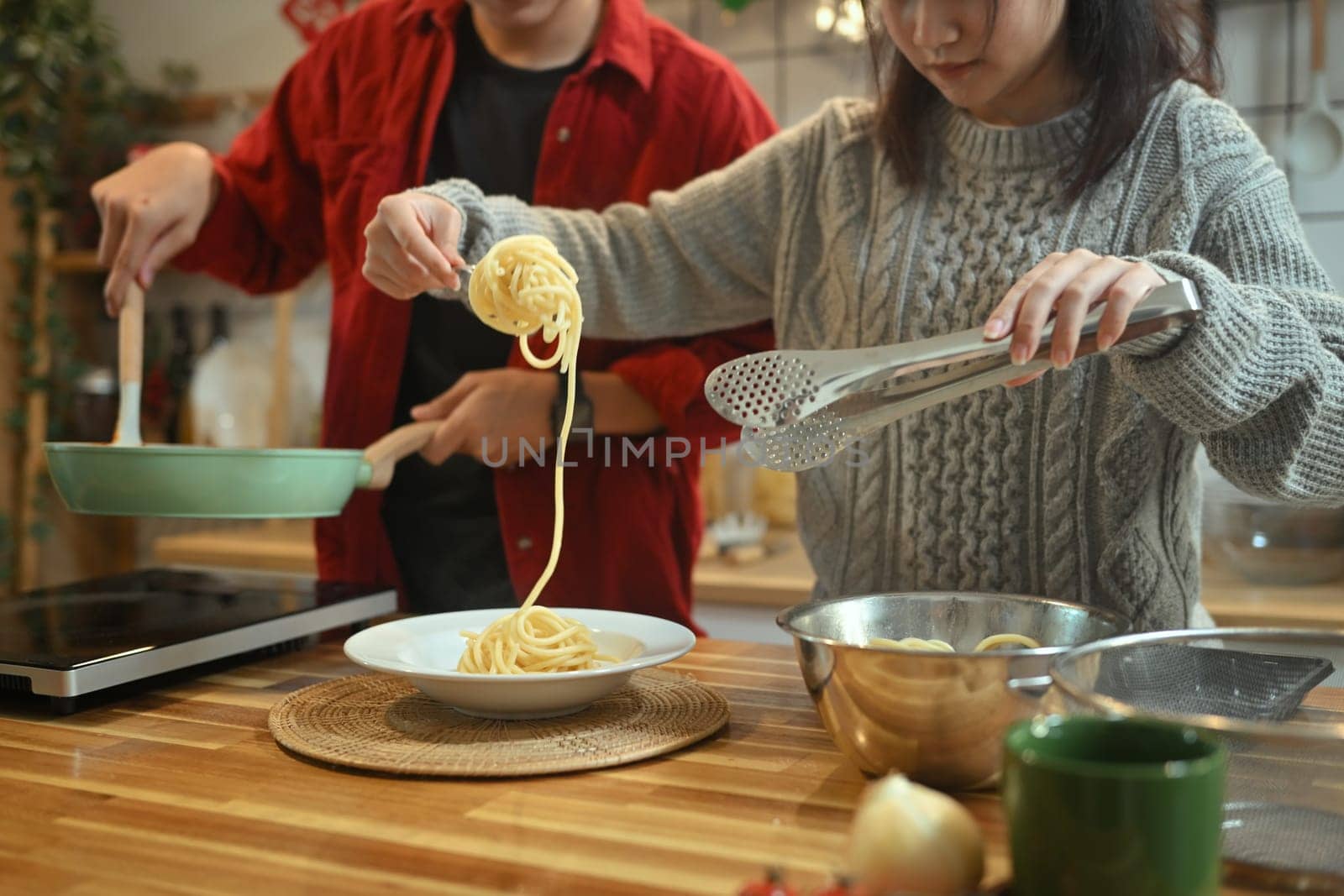 Young married beautiful couple in sweaters preparing dinner on Christmas Day in kitchen.