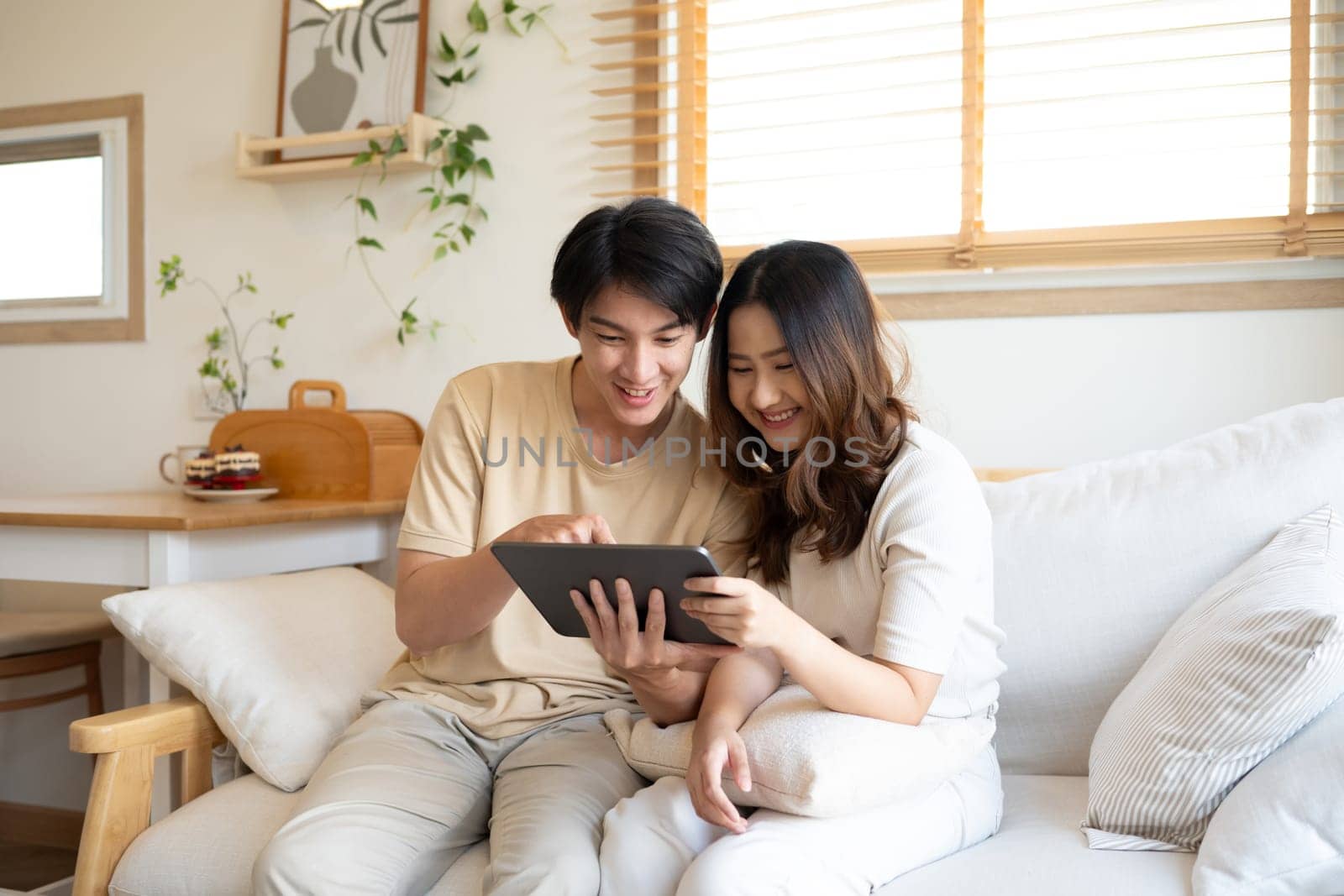 Happy young couple in casual wears watching online content on digital tablet at home.