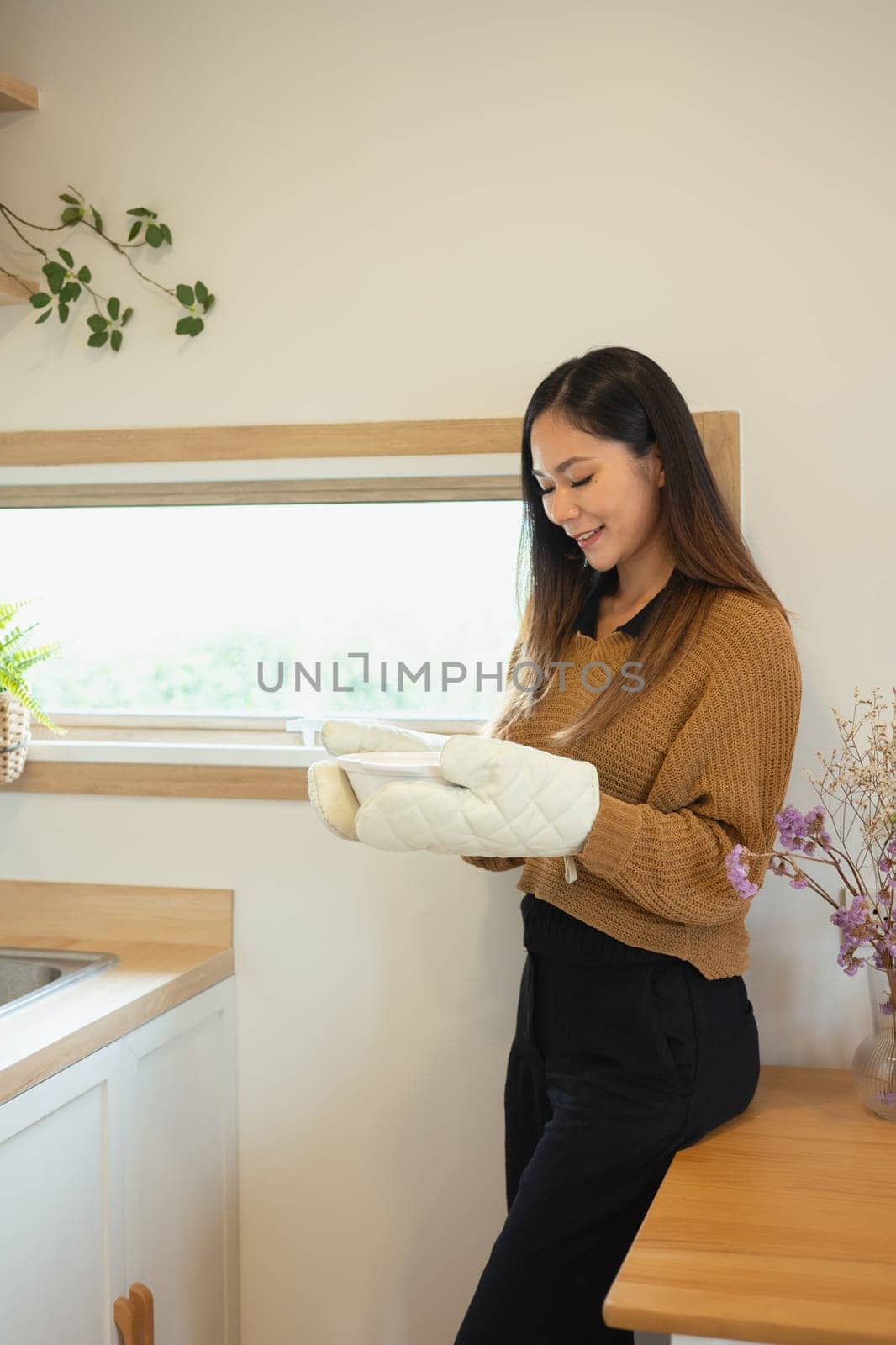 Beautiful woman holding a freshly baked dish with oven mitts, ready to serve.