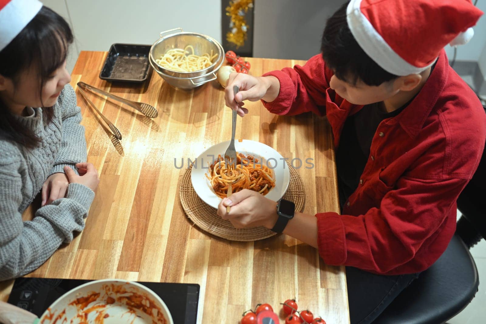 Above view of young couple in Santa hats enjoying a warm holiday dinner in the kitchen.