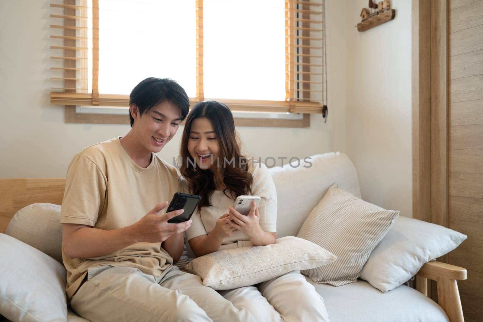 Relaxed asian couple watching online content on a smart phone in the living room.