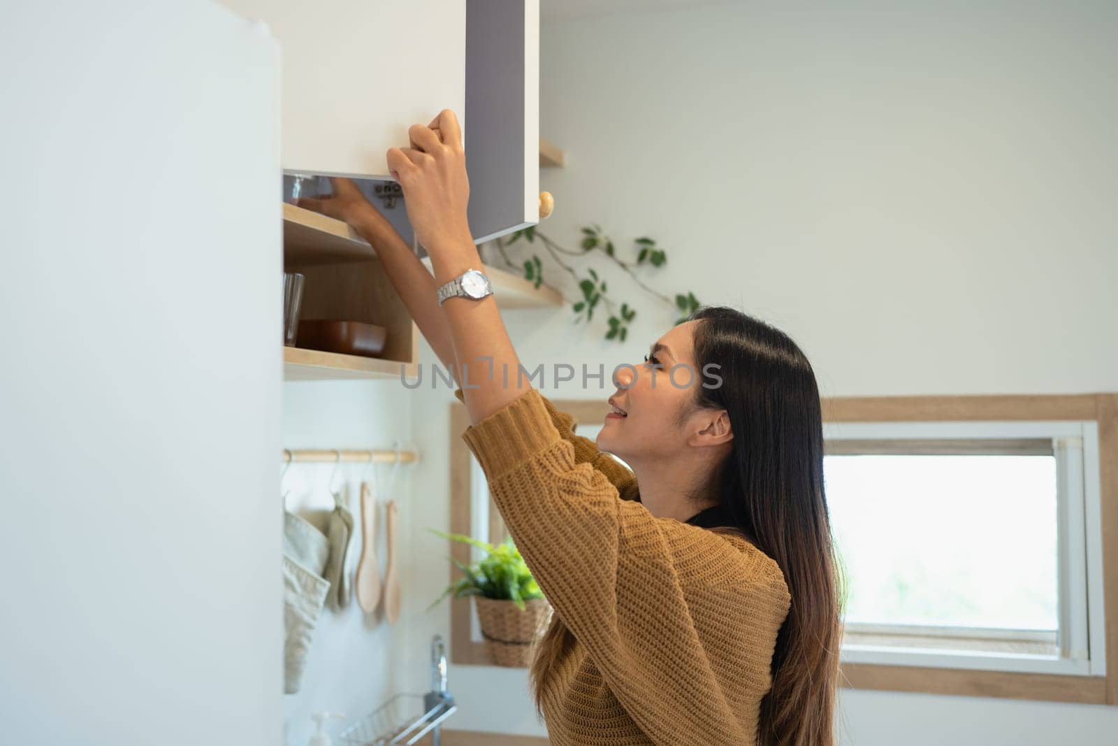 Beautiful woman reaching for ingredients in upper kitchen cabinets.