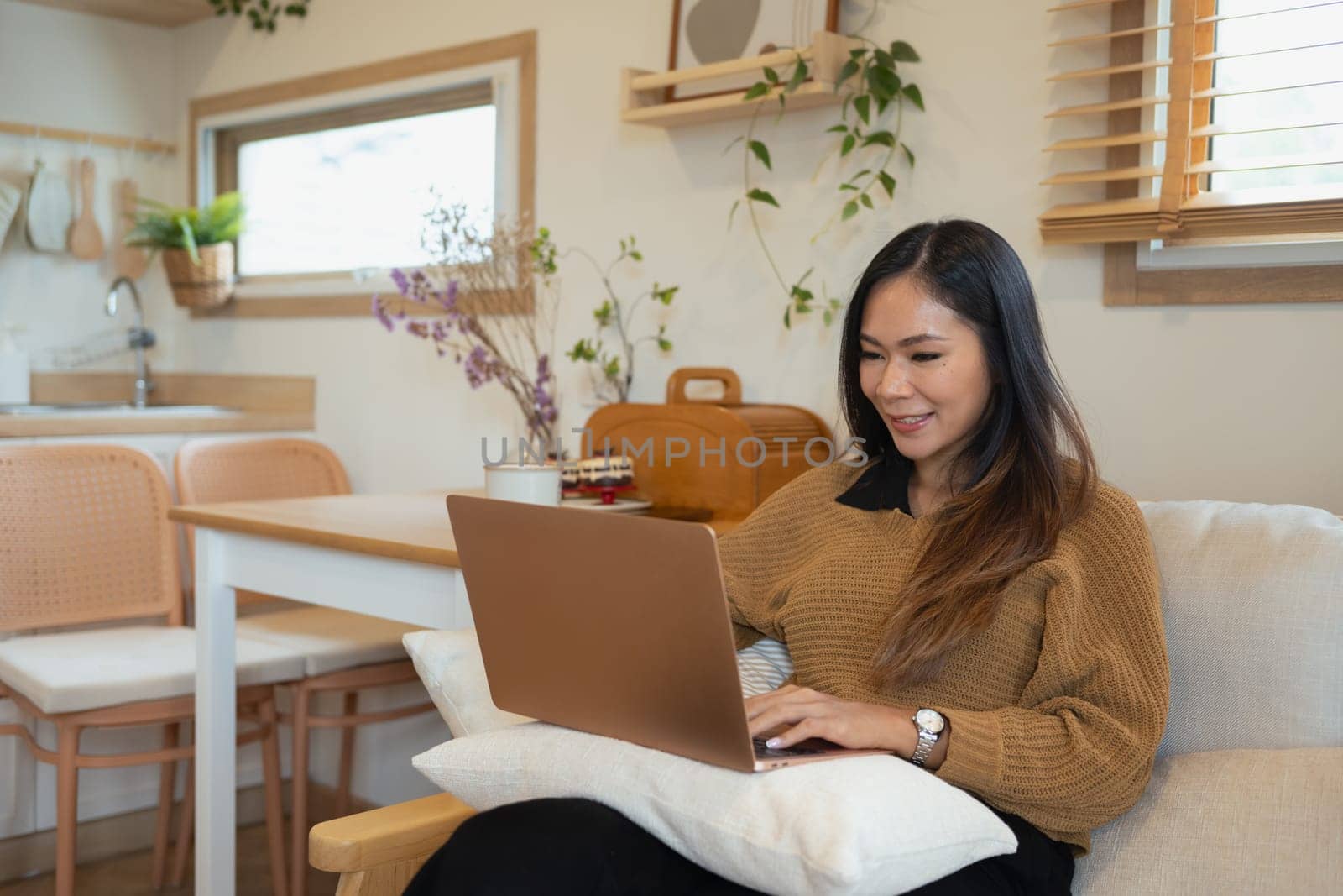 Smiling young adult woman browsing internet on her laptop at home.