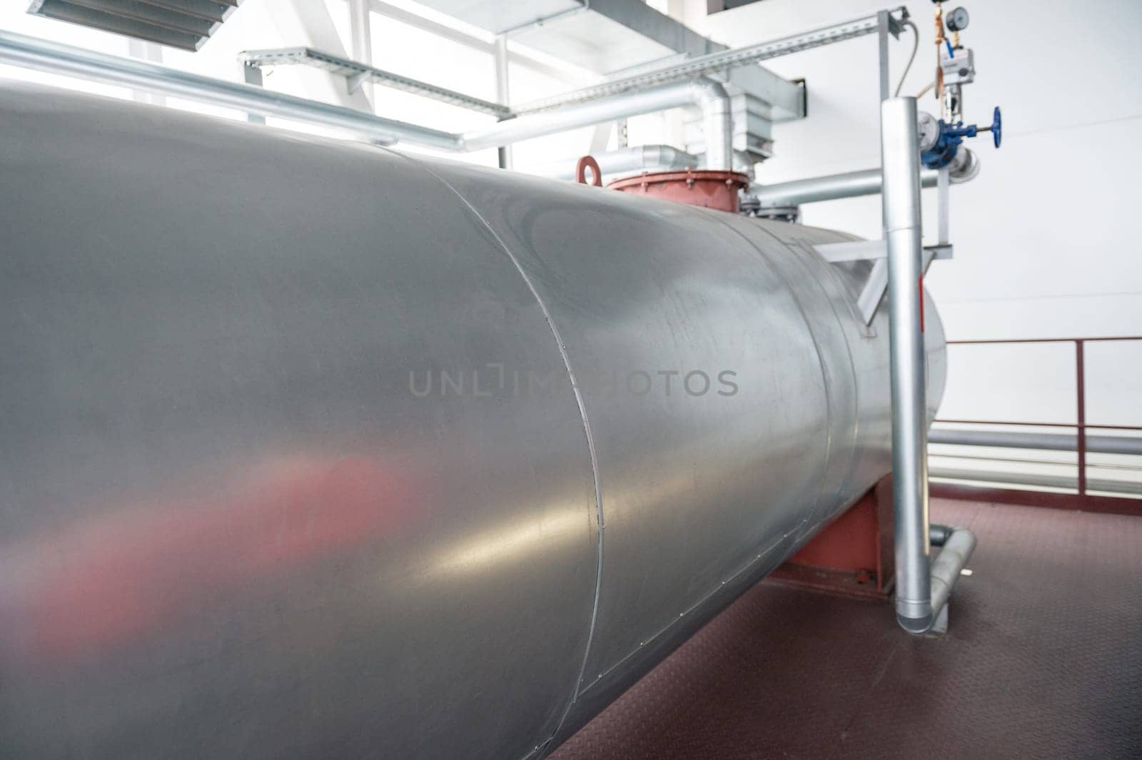 Outdoor Atmospheric Pressure deaerator. Close-up of a large metallic tank in an industrial facility, featuring pipes and equipment.