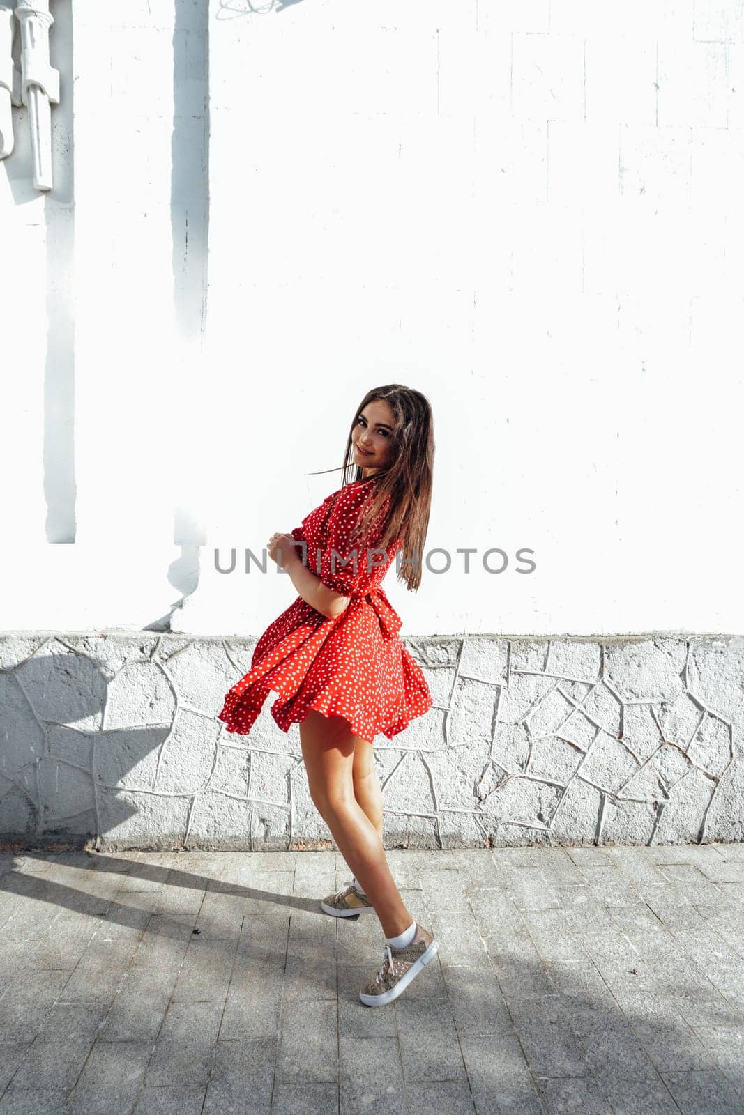 Beautiful woman in a red summer dress walking through the streets of the city