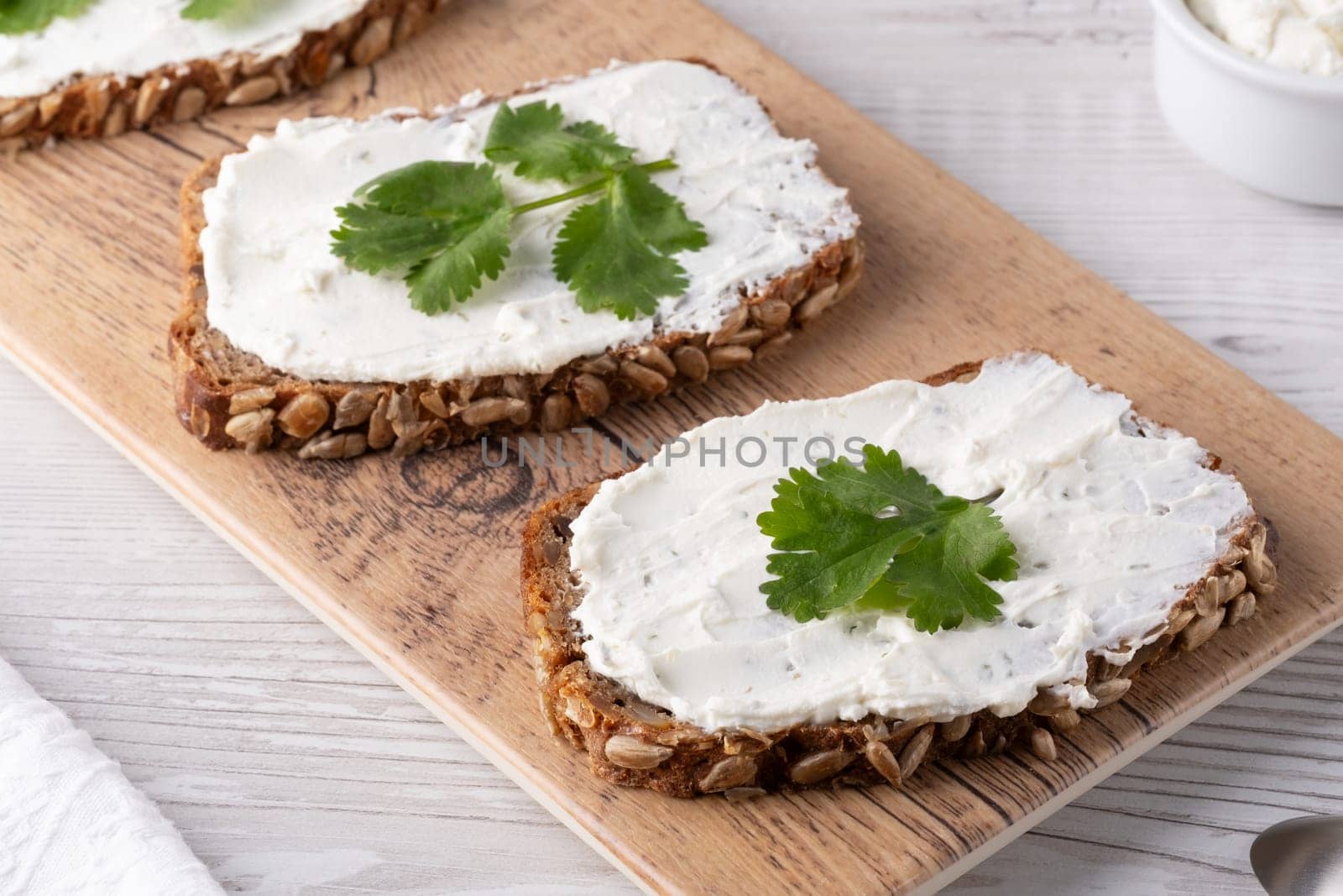 Freshly prepared slices of hearty multigrain bread topped with creamy spread and cilantro leaves on a wooden board.