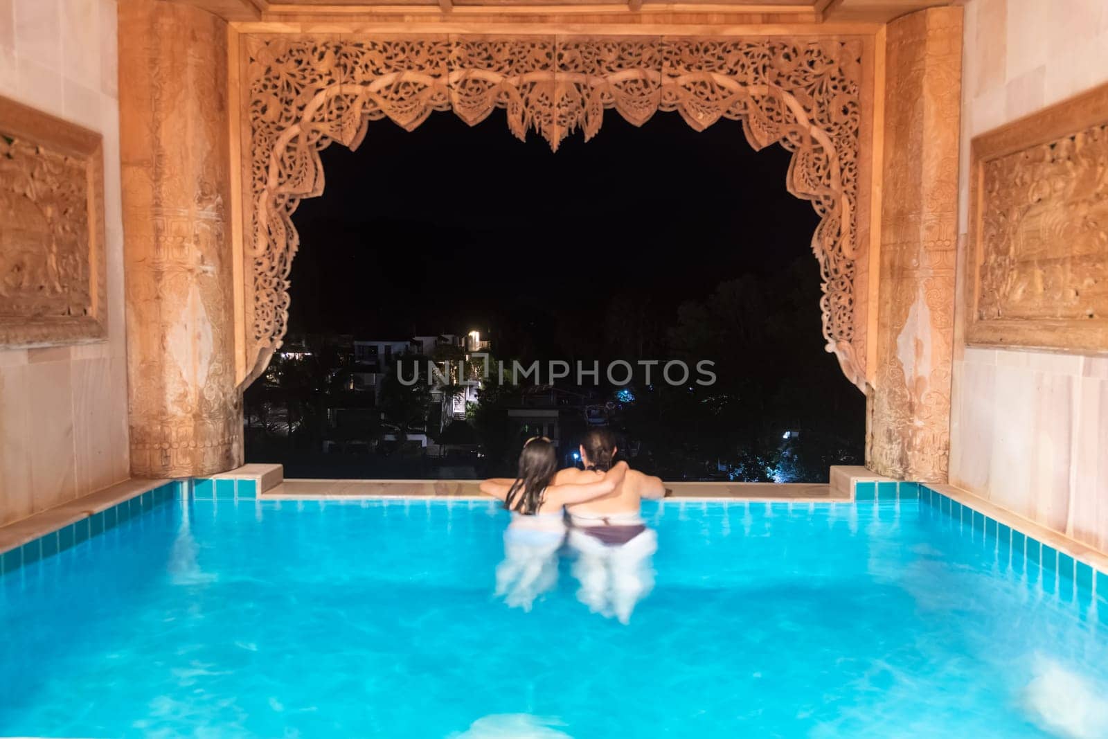 Two individuals delight in a peaceful evening beside a lovely pool that overlooks the sparkling city lights