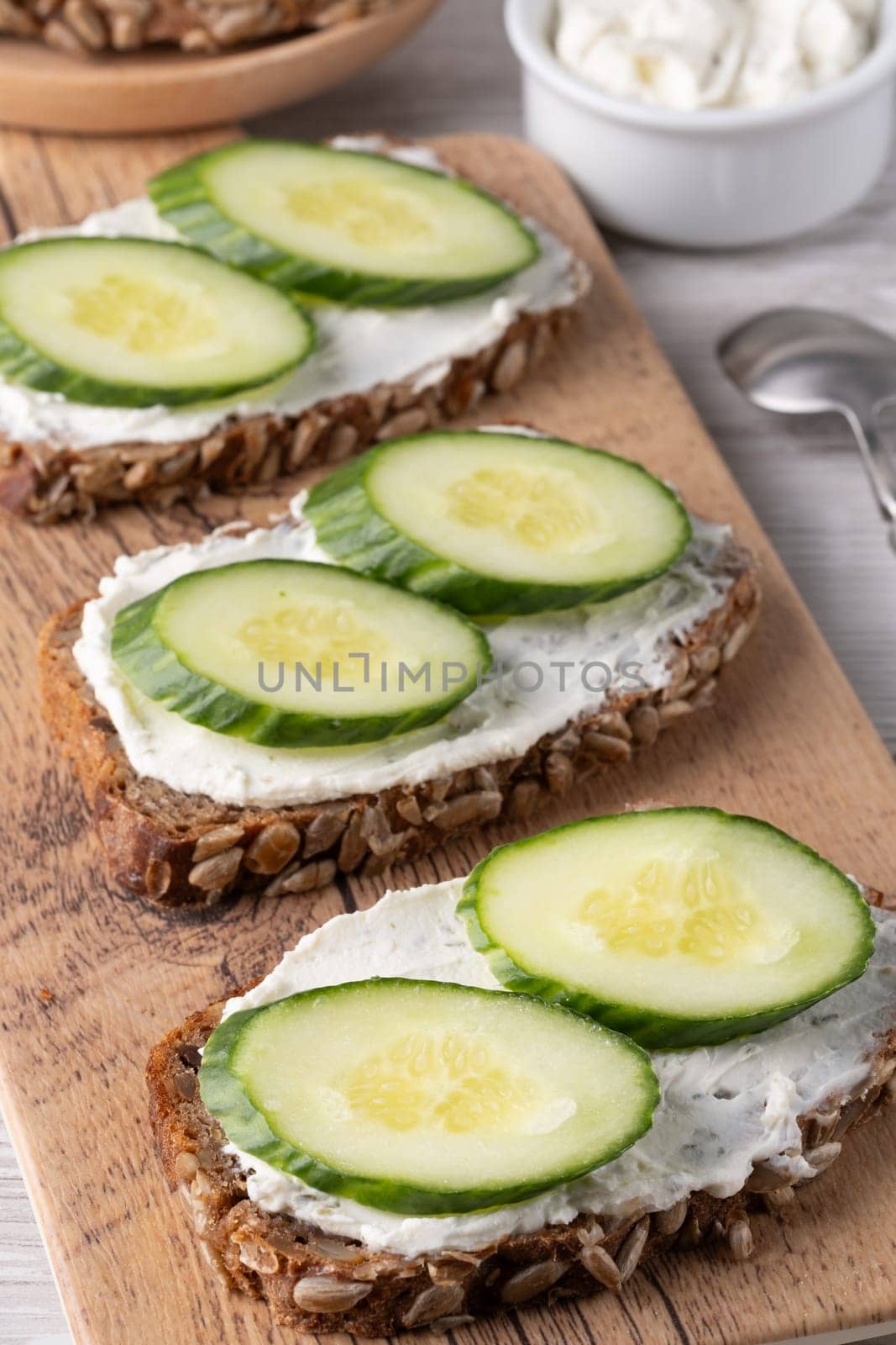 Slices of whole grain bread topped with cream cheese and fresh cucumber arranged beautifully at a rustic wooden table.