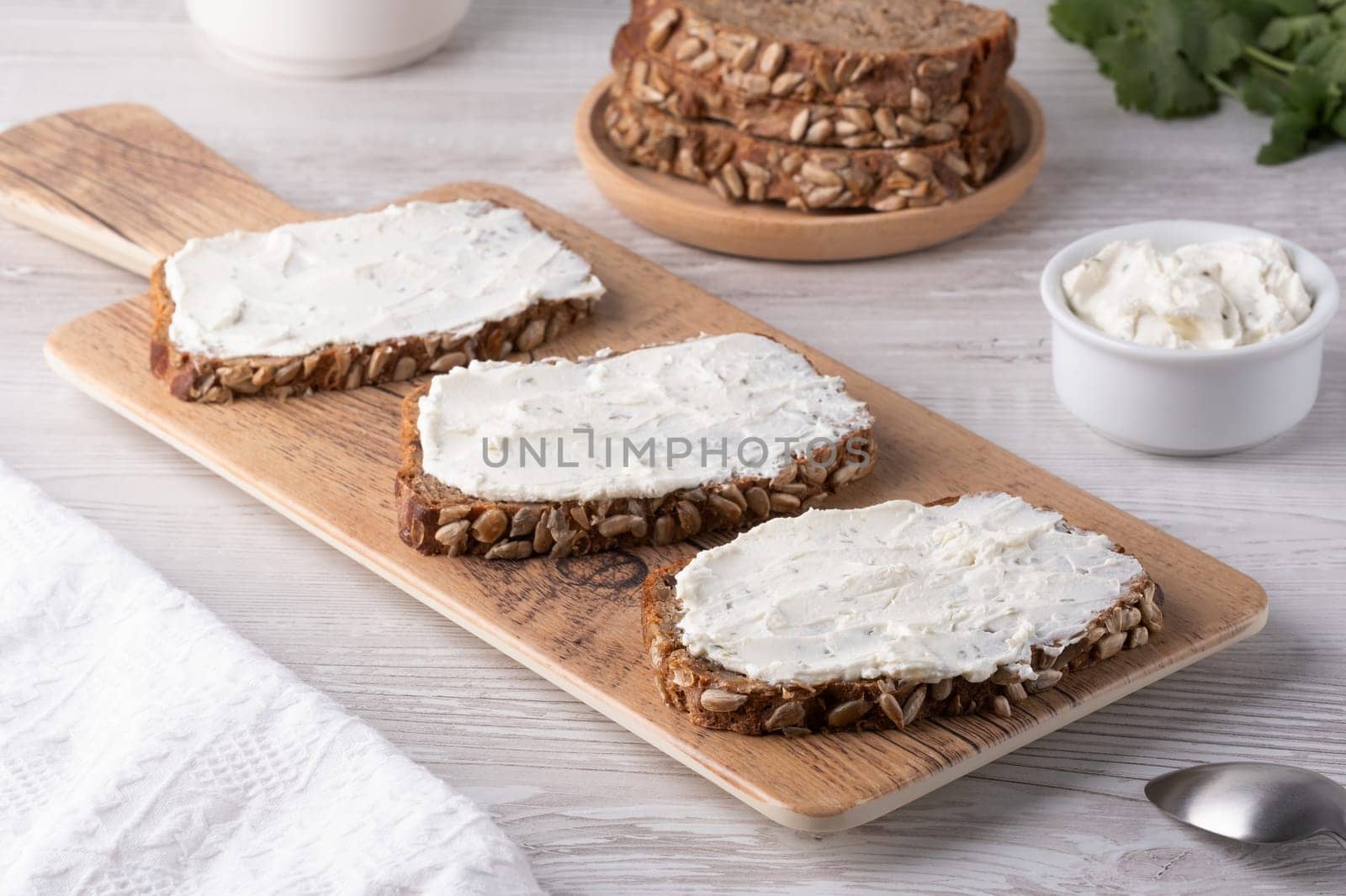 Slices of whole grain bread topped with cream cheese on a wooden cutting board in a cozy kitchen setting.