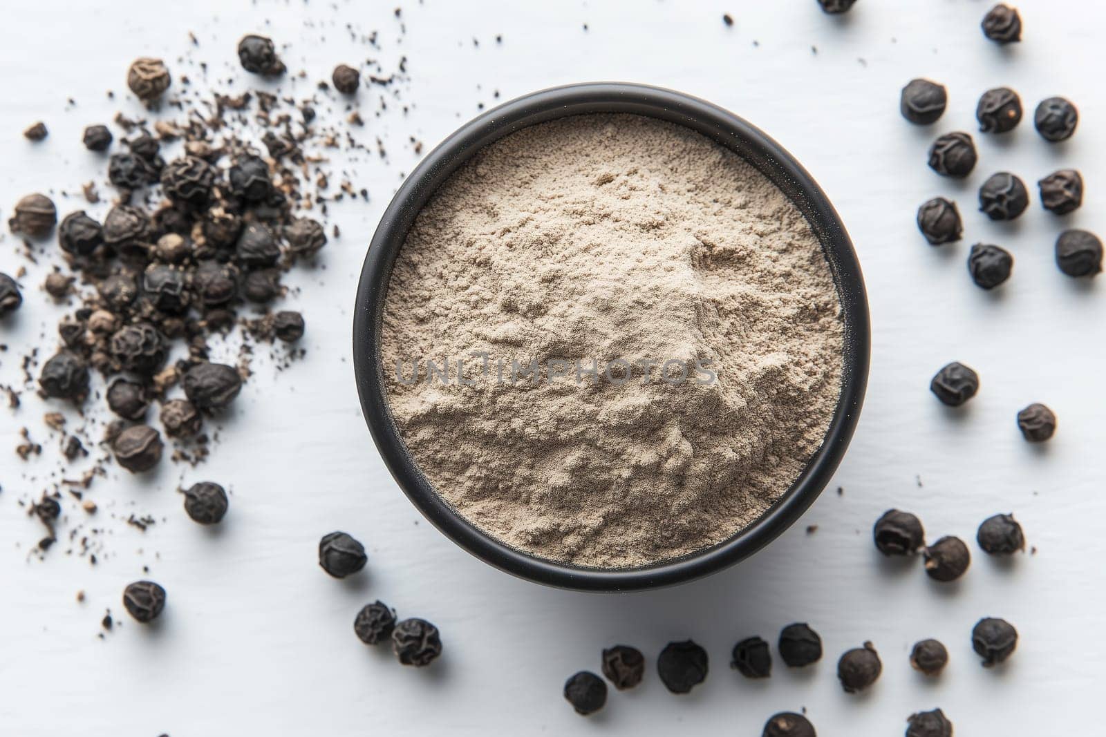 A bowl of finely ground black pepper sits on a white surface, surrounded by whole peppercorns. This arrangement showcases the spice's versatility in cooking.