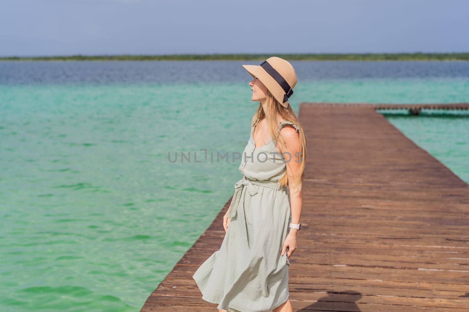 Female tourist in a turquoise dress standing on a wooden pier over the turquoise waters of Bacalar Lake, Mexico. Peaceful tropical travel destination concept.