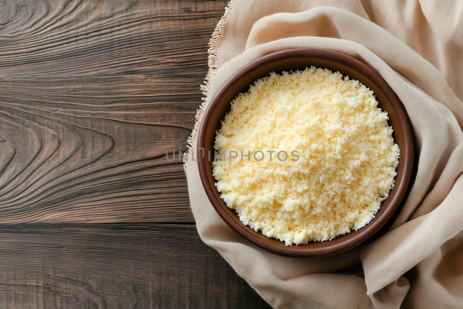 A bowl filled with fine cornmeal is displayed on a wooden surface, accompanied by a beige cloth. The scene highlights the rustic charm and simplicity of the ingredients.