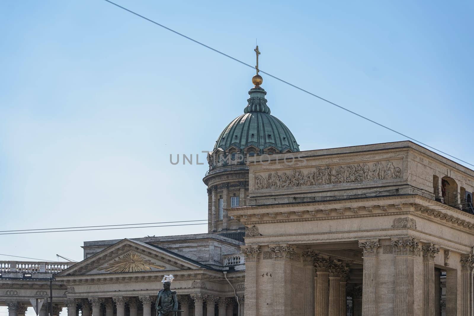 Close-up of a historic cathedral's architectural details, featuring a prominent dome topped with a cross, under a clear blue sky. Classical design elements convey grandeur and tradition