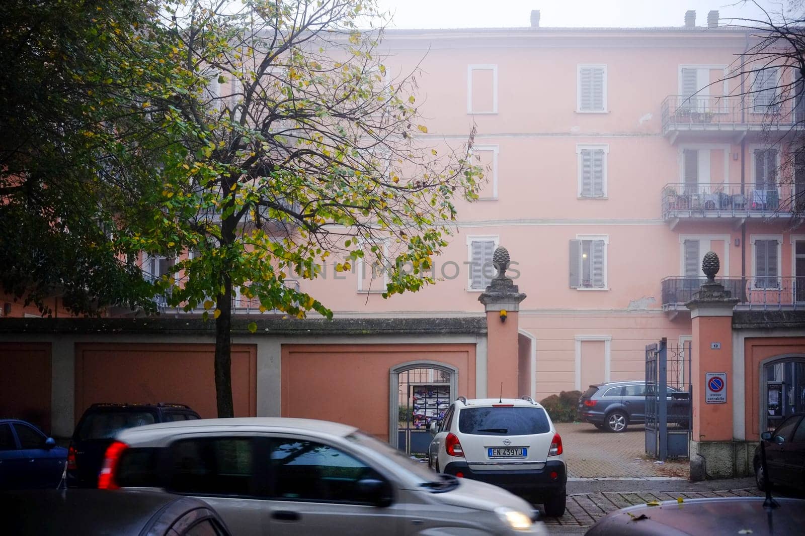Cremona, Lombardy, Italy - November 7th 2024 White cars passing by a pink residential building on a foggy autumn day