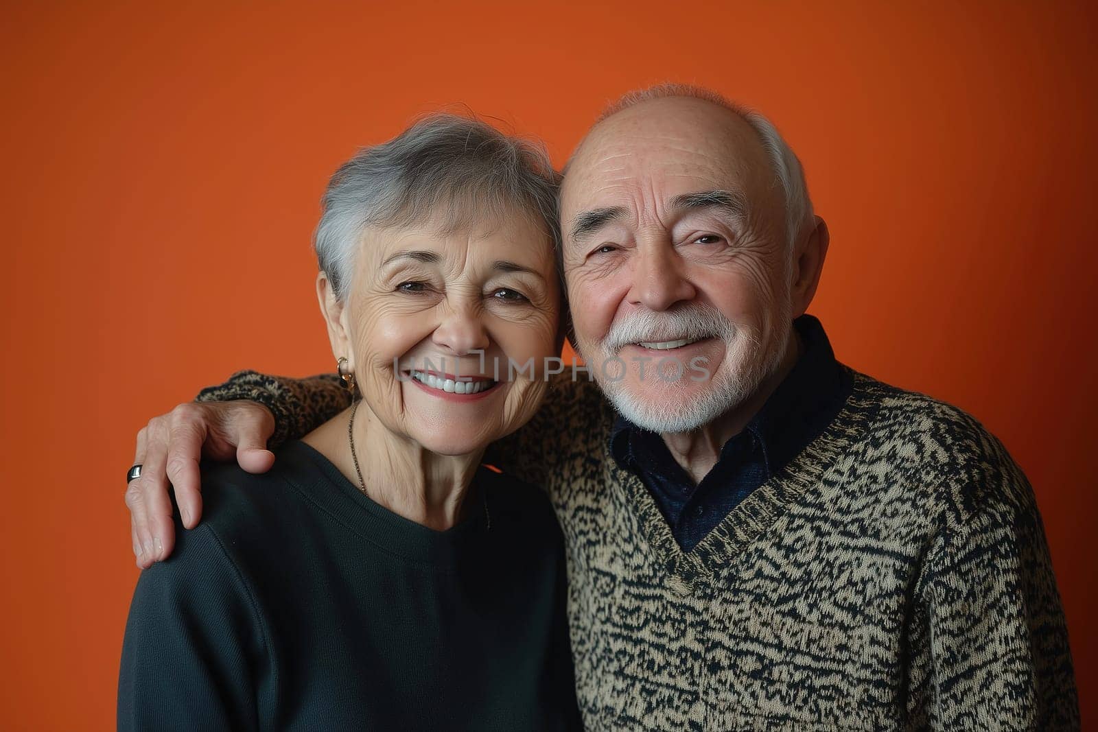 An elderly couple stands close, smiling warmly at the camera with their arms around each other.
