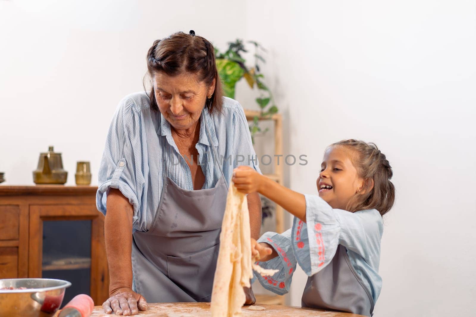 Cheerful girl proudly holds up flattened dough while baking with grandmother, creating warm and joyful moment in heart of their cozy home