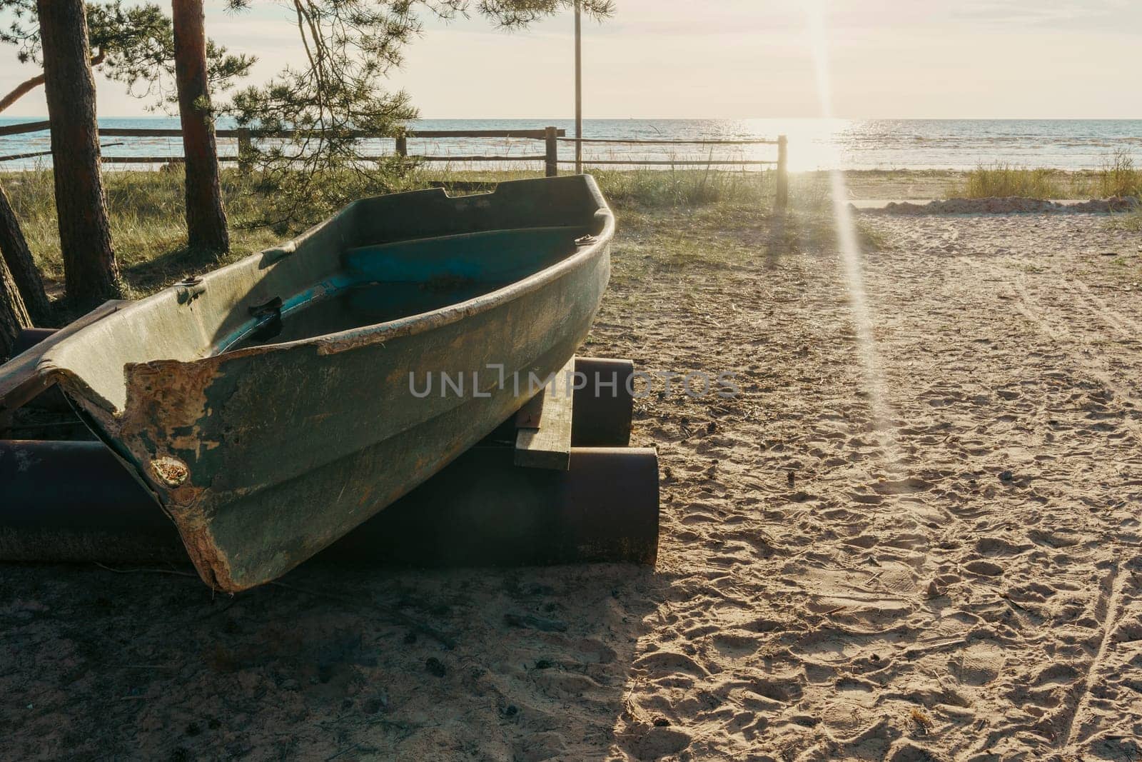 An old boat rests on a sandy beach as the sun sets over the water, casting warm rays and creating a peaceful and serene atmosphere in a rustic coastal scene