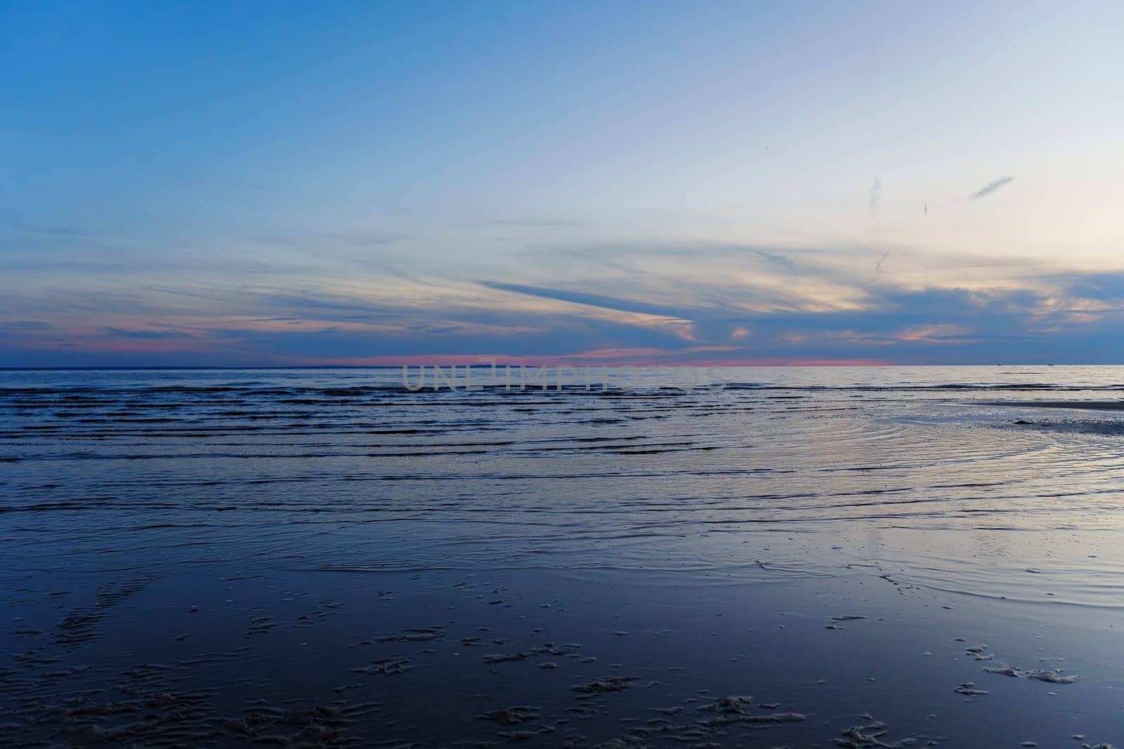 A peaceful sunset over a calm ocean with gentle waves and a colorful sky, creating a tranquil and scenic landscape. The image captures the beauty of twilight with no people in view.