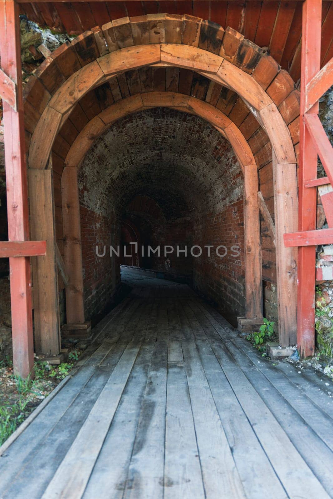 An arched entrance leading into a dark tunnel constructed with wood and stone inside a historic fortress. The dim passageway evokes a sense of mystery and medieval architecture
