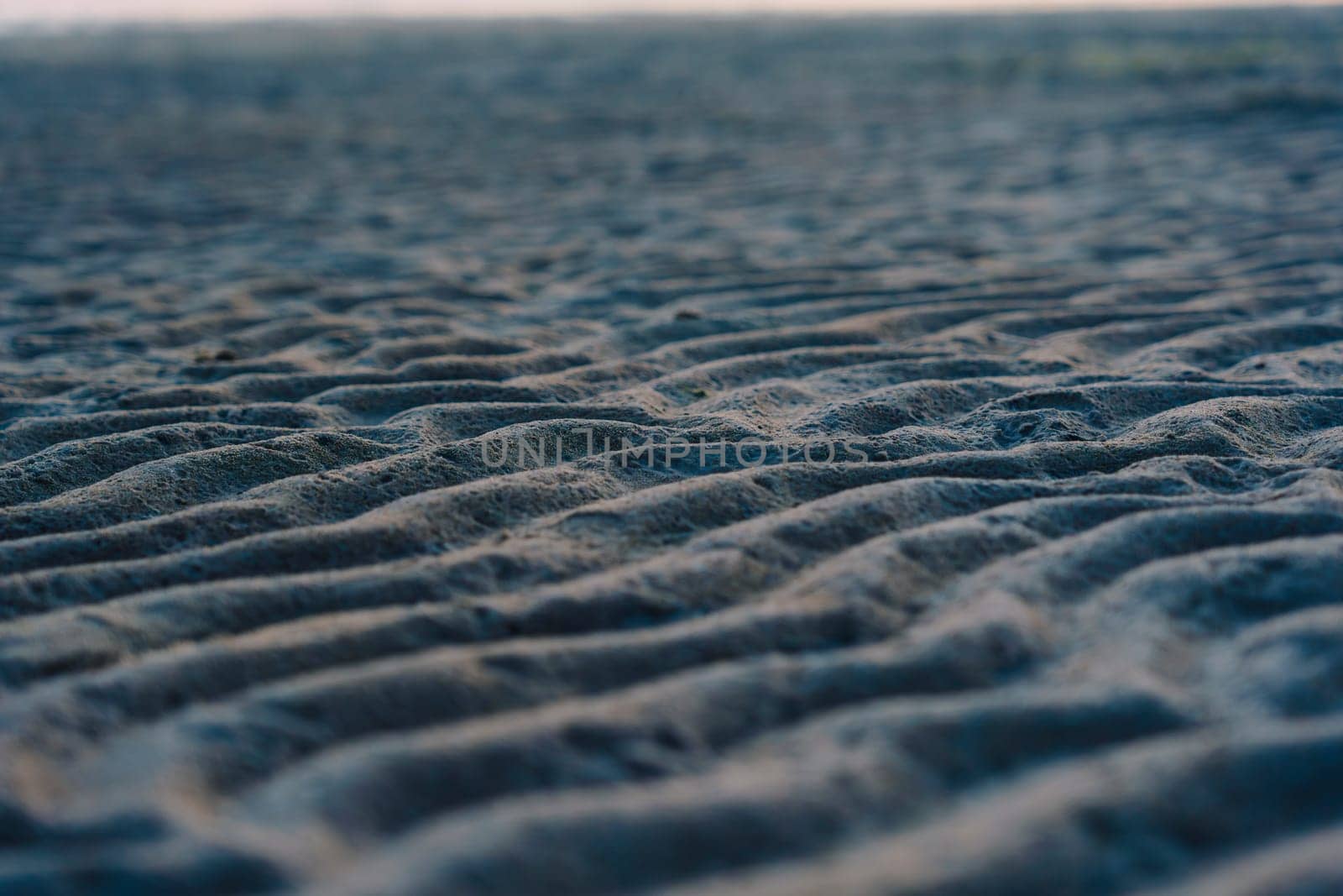 A close-up of rippled sand patterns on a beach at low tide, capturing natural textures and wavy details in a tranquil coastal scene