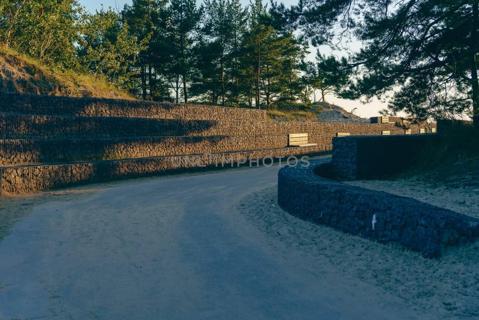 Serene outdoor path lined with stone retaining walls and surrounded by trees, winding through a park in soft, golden evening light