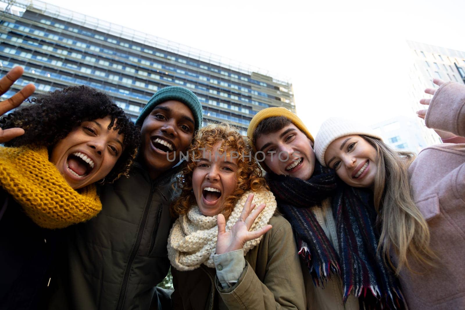 Group of happy multiracial friends looking at camera waving hand during winter time in the city. Lifestyle portrait concept.