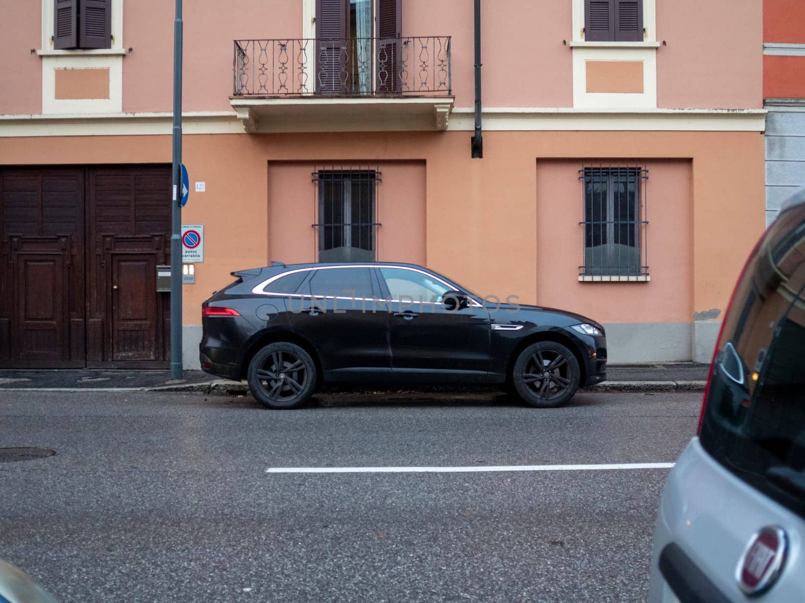 Cremona, Lombardy, Italy October 15th 2024 A black jaguar f pace is parked on a narrow street in front of a typical italian building with an orange facade