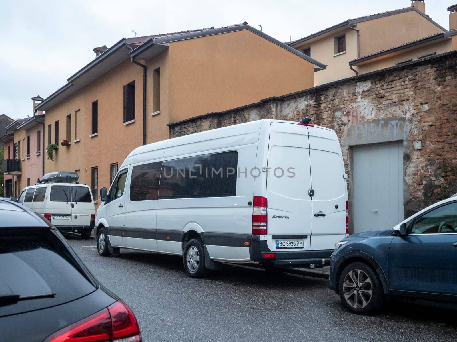 Cremona, Lombardy, Italy October 15th 2024 White mercedes benz sprinter van parked on a narrow street in a residential area of an italian town, showcasing urban parking challenges