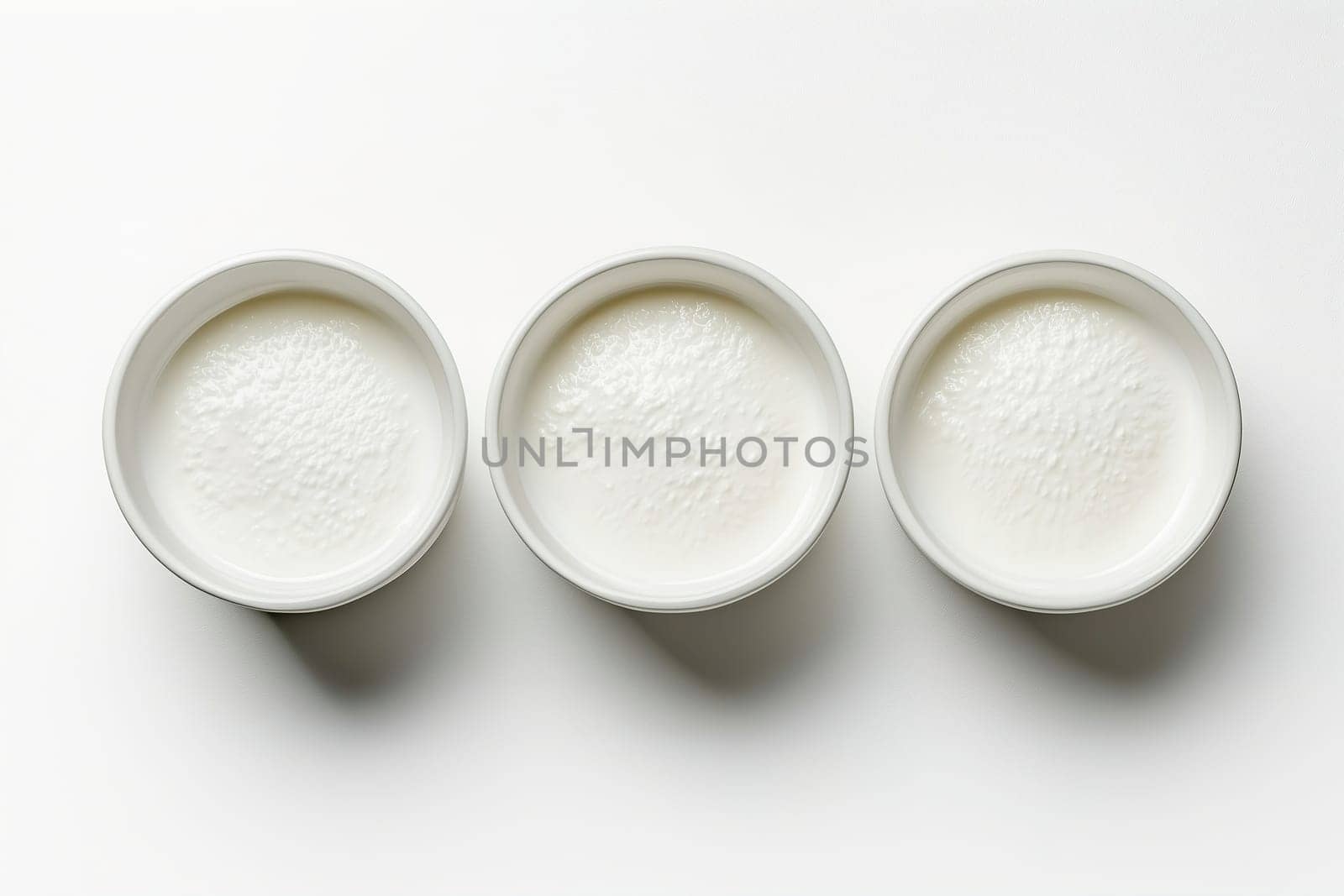 Three small white bowls are placed side by side, each containing a smooth, creamy substance. The minimalist arrangement focuses on texture and color in a well-lit setting.
