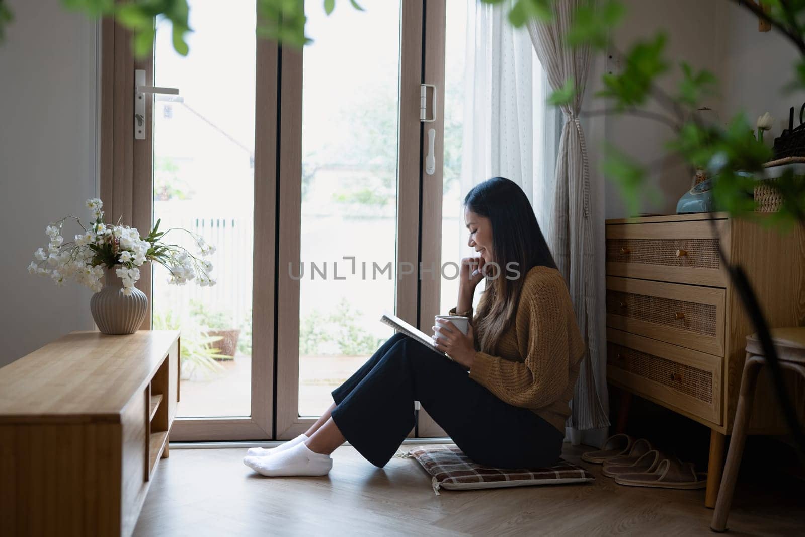 Peaceful young woman writing her diary and relaxing with a warm drink by the window.