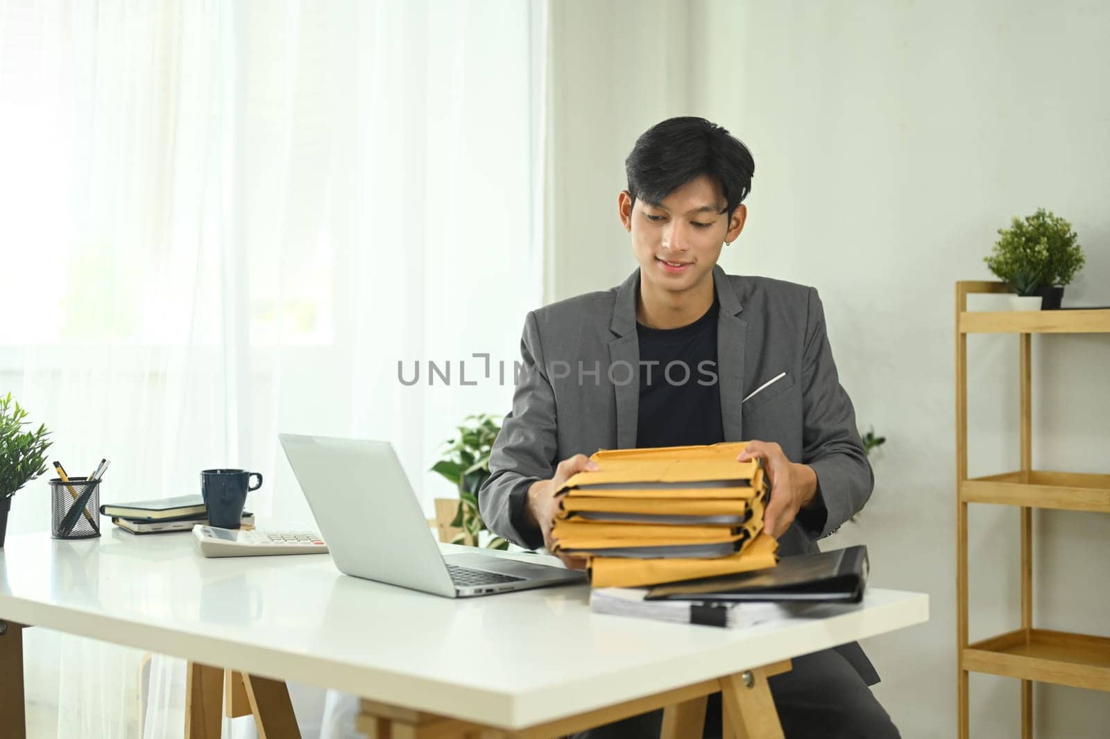 Young businessman organizing important documents in envelopes at office desk.