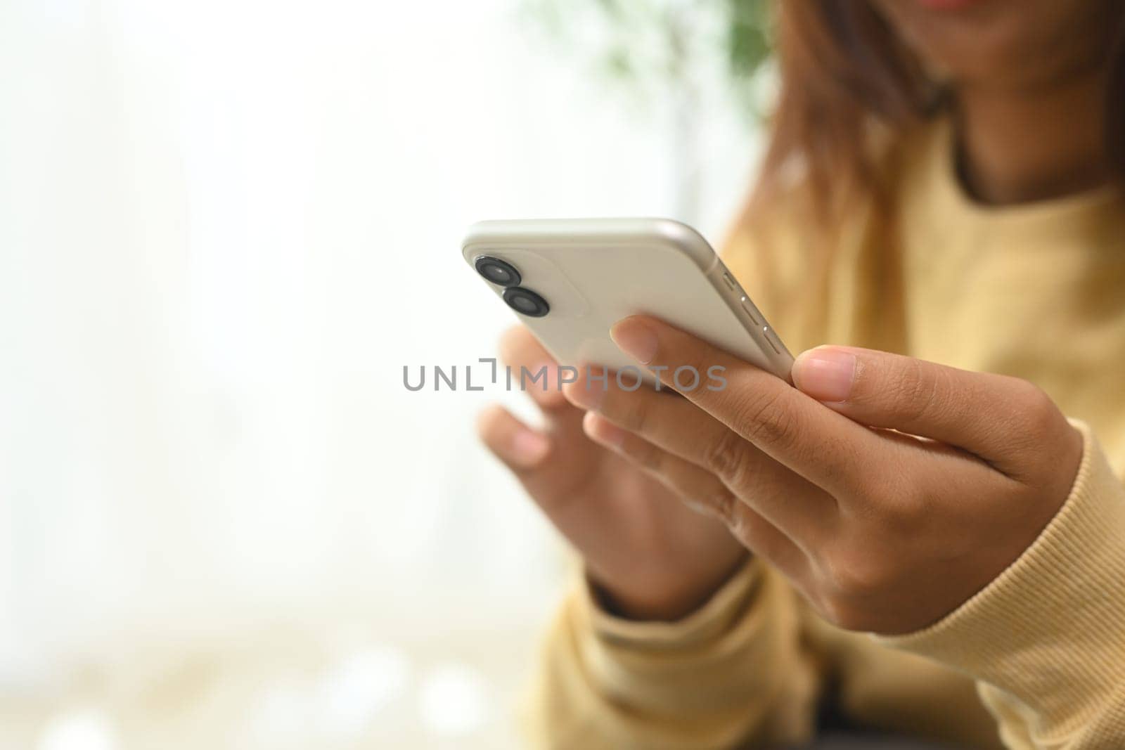 Close up of woman in yellow sweater typing message on her smartphone.