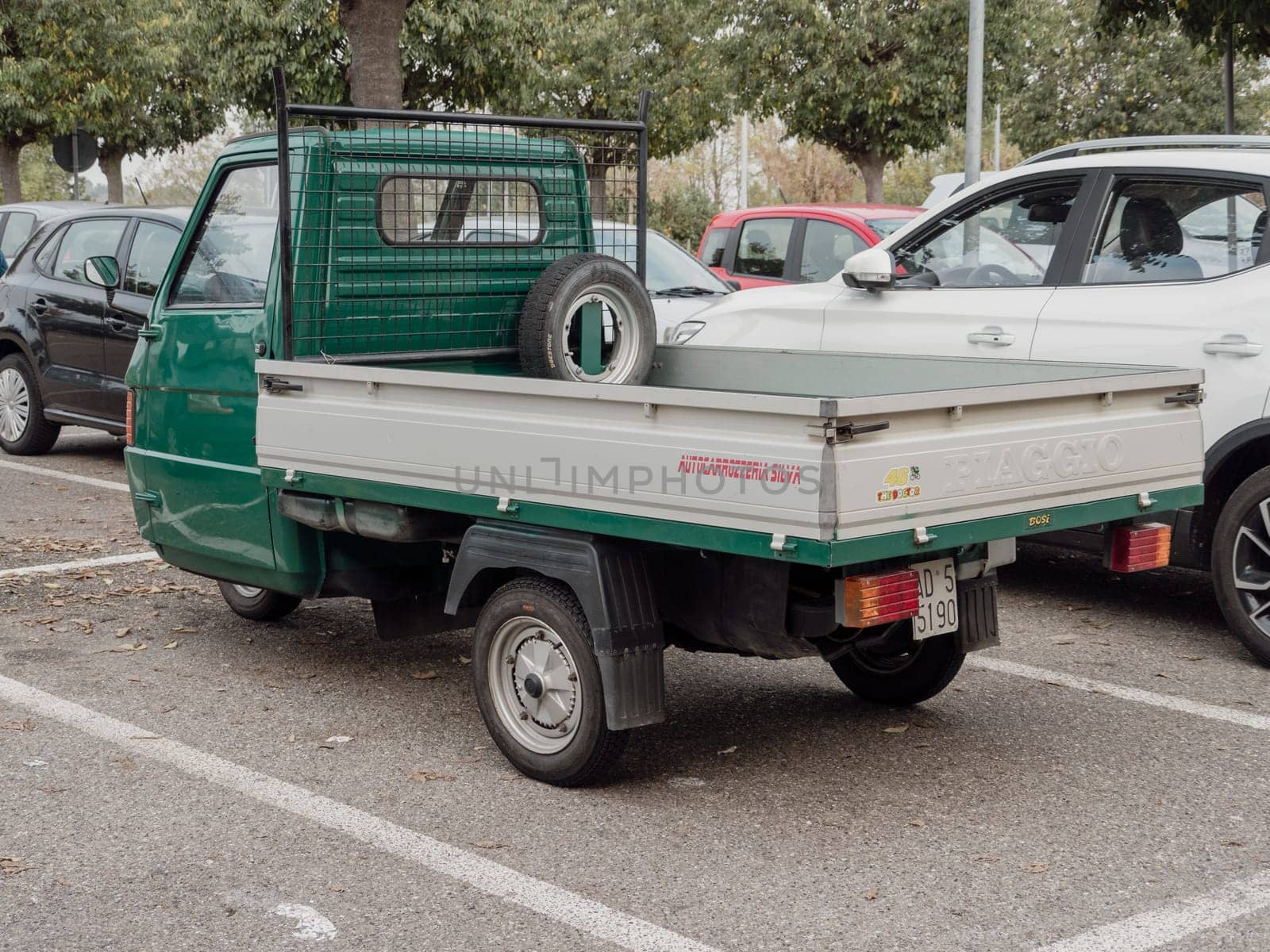Arquato, PC, italy - October 31st 2024 Small green commercial vehicle Ape piaggio porter parked in an outdoor parking lot, showing its rear part with spare wheel and license plate