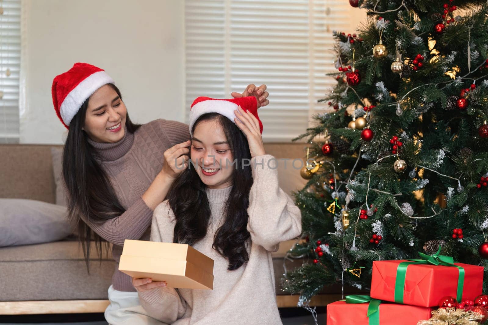 Happy young women enjoying Christmas day, exchanging gifts by a beautifully decorated tree in a warm, festive atmosphere.