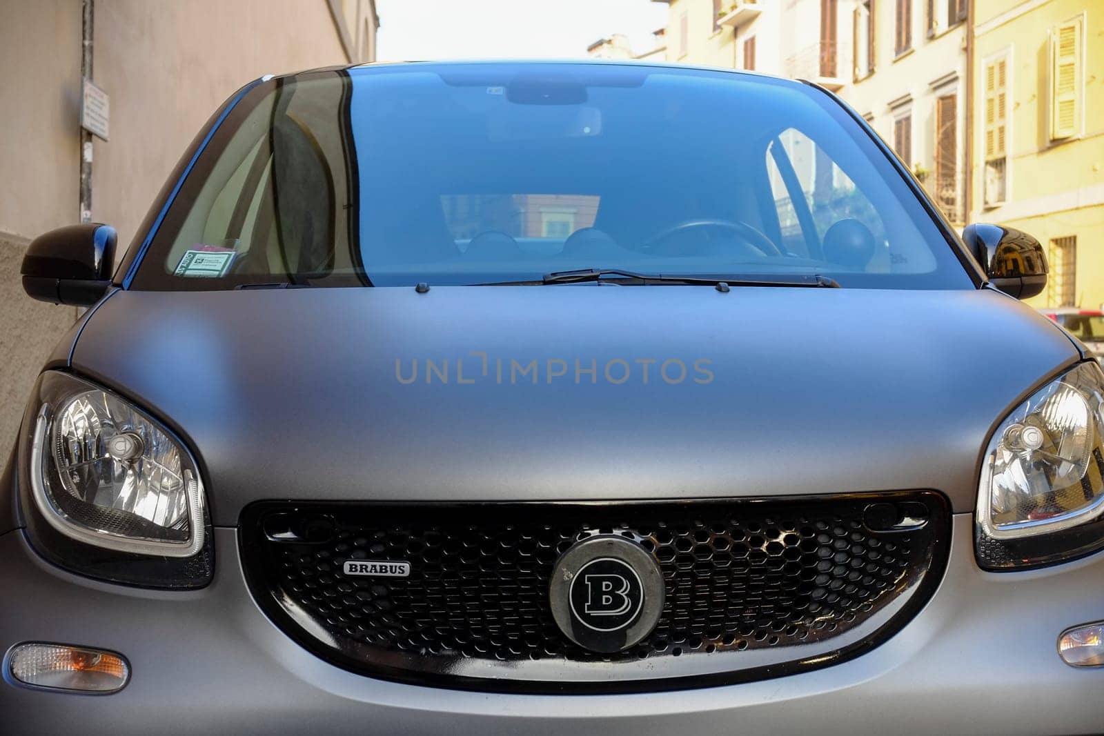 Cremona, Lombardy, Italy - November 7th 2024 Front view of a smart brabus parked on a narrow street in an old european city center, reflecting surrounding buildings on its windshield
