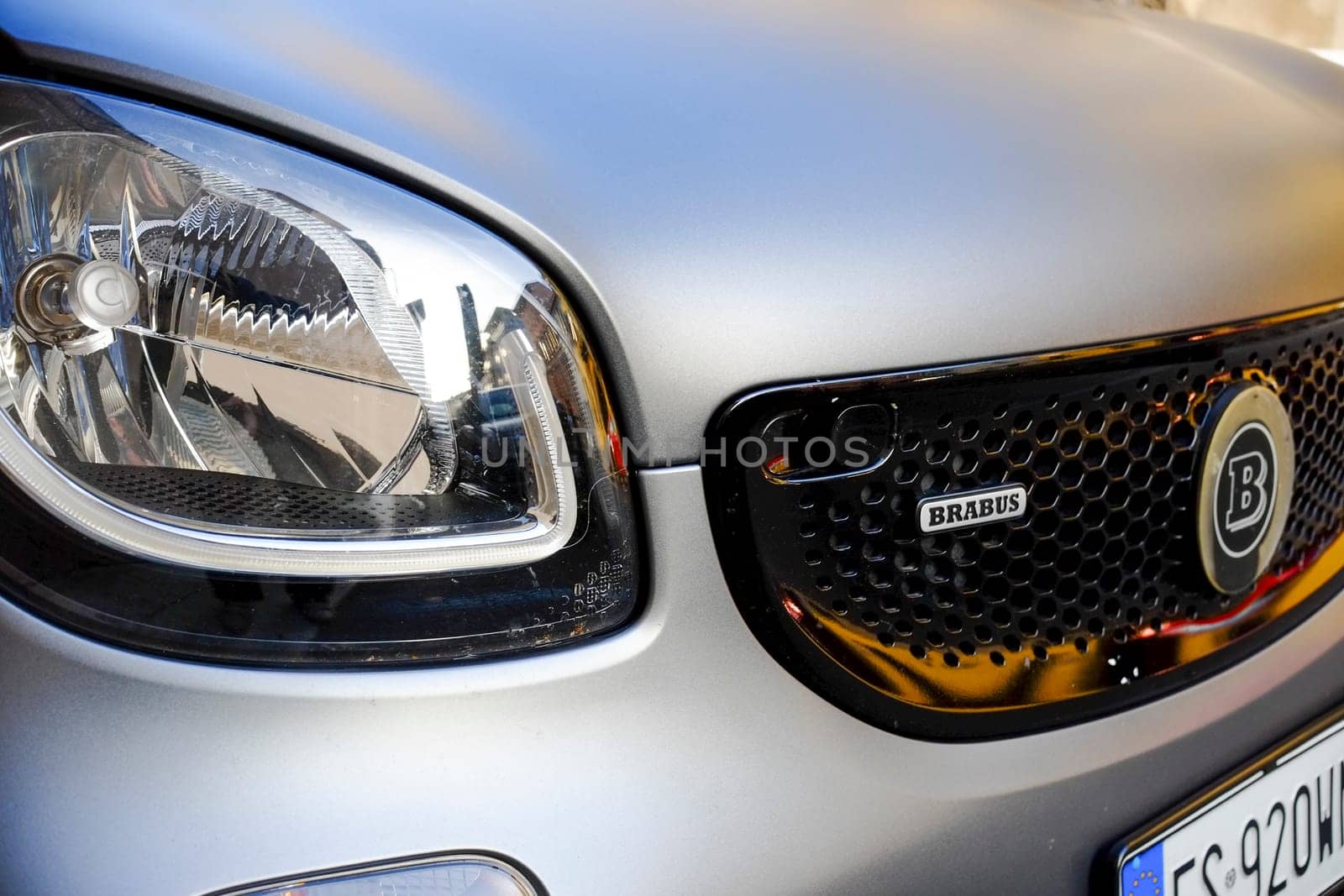 Cremona, Lombardy, Italy - November 7th 2024 Polished silver smart car showcasing brabus tuning, with headlight reflecting surrounding cityscape