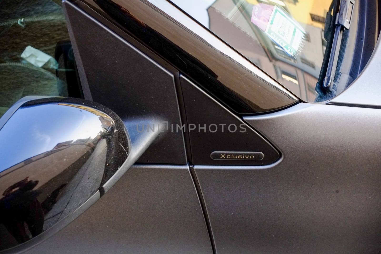 Cremona, Lombardy, Italy - November 7th 2024 Close-up of an xclusive badge on a gray car's door, with the rearview mirror reflecting a street view