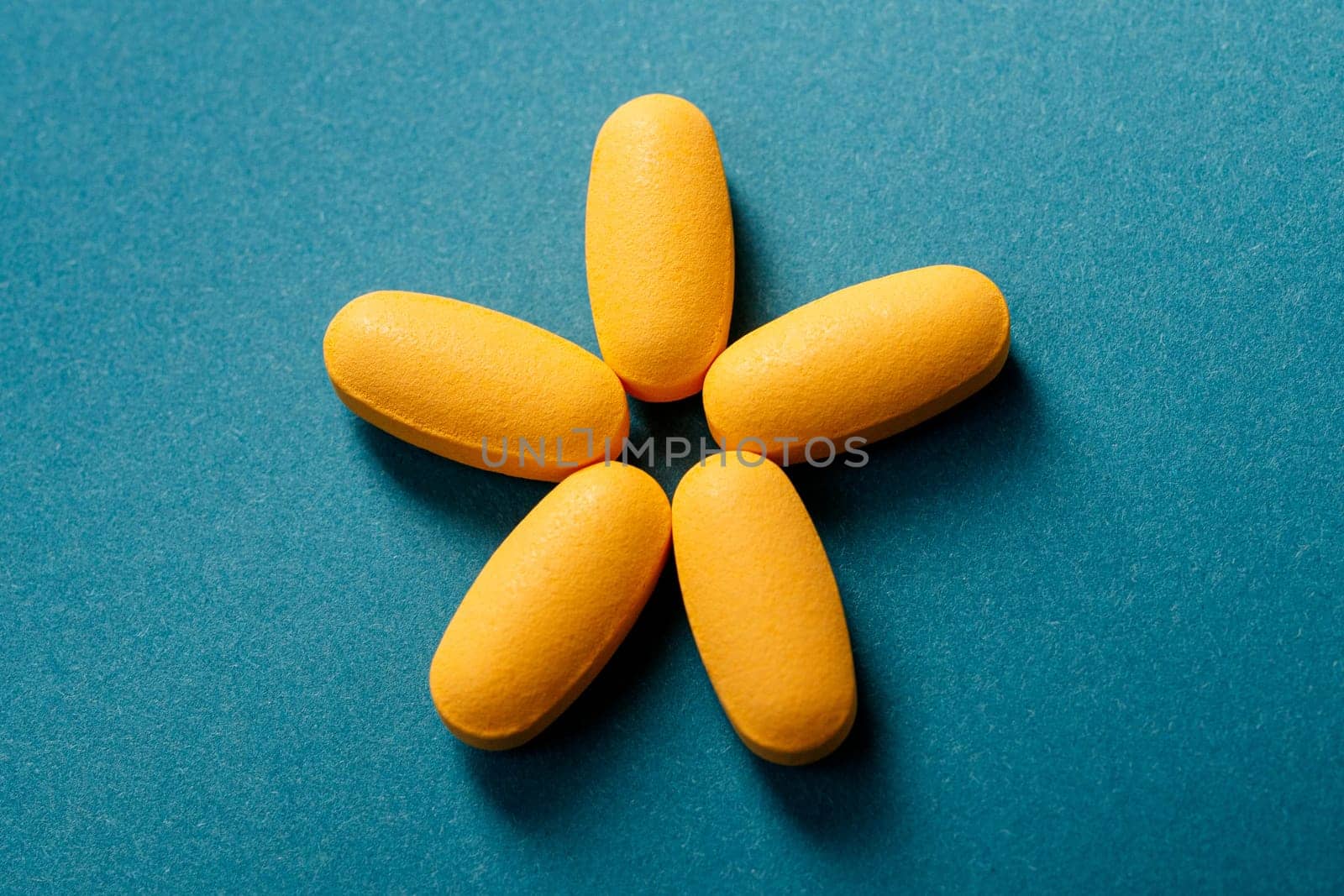 Close up of 5 yellow pills or Dietary supplement laid out in the shape of a star on blue background.