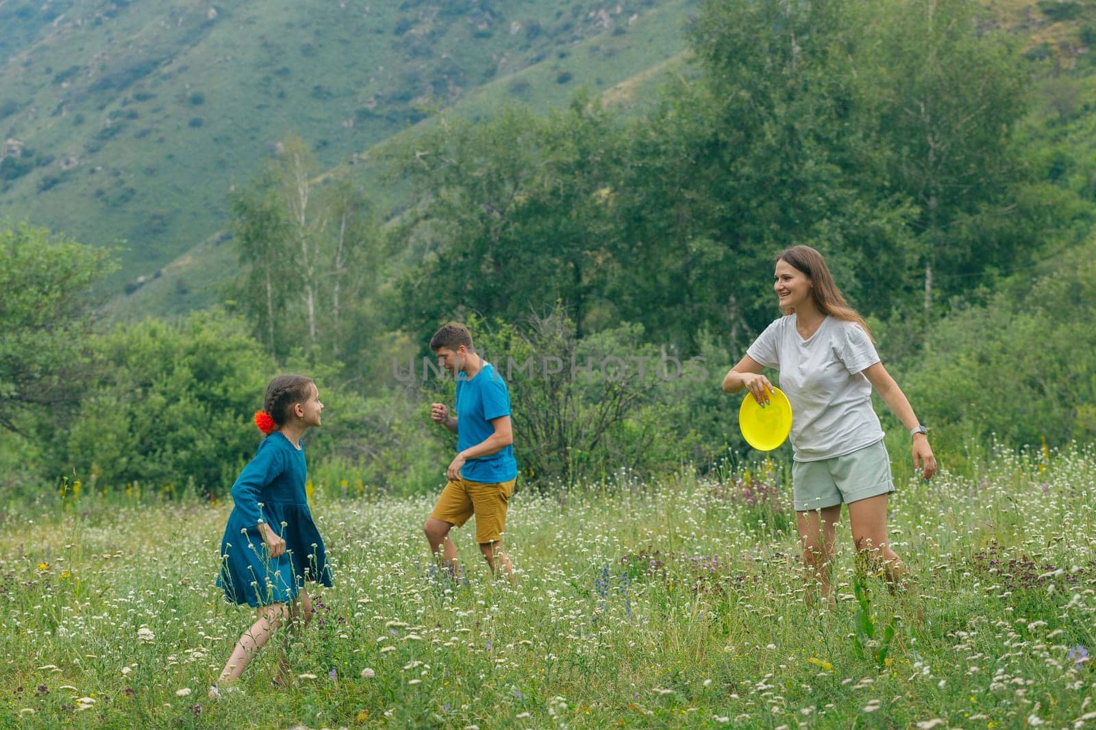 Children and an adult joyfully play frisbee in a vibrant meadow with stunning mountains in the background